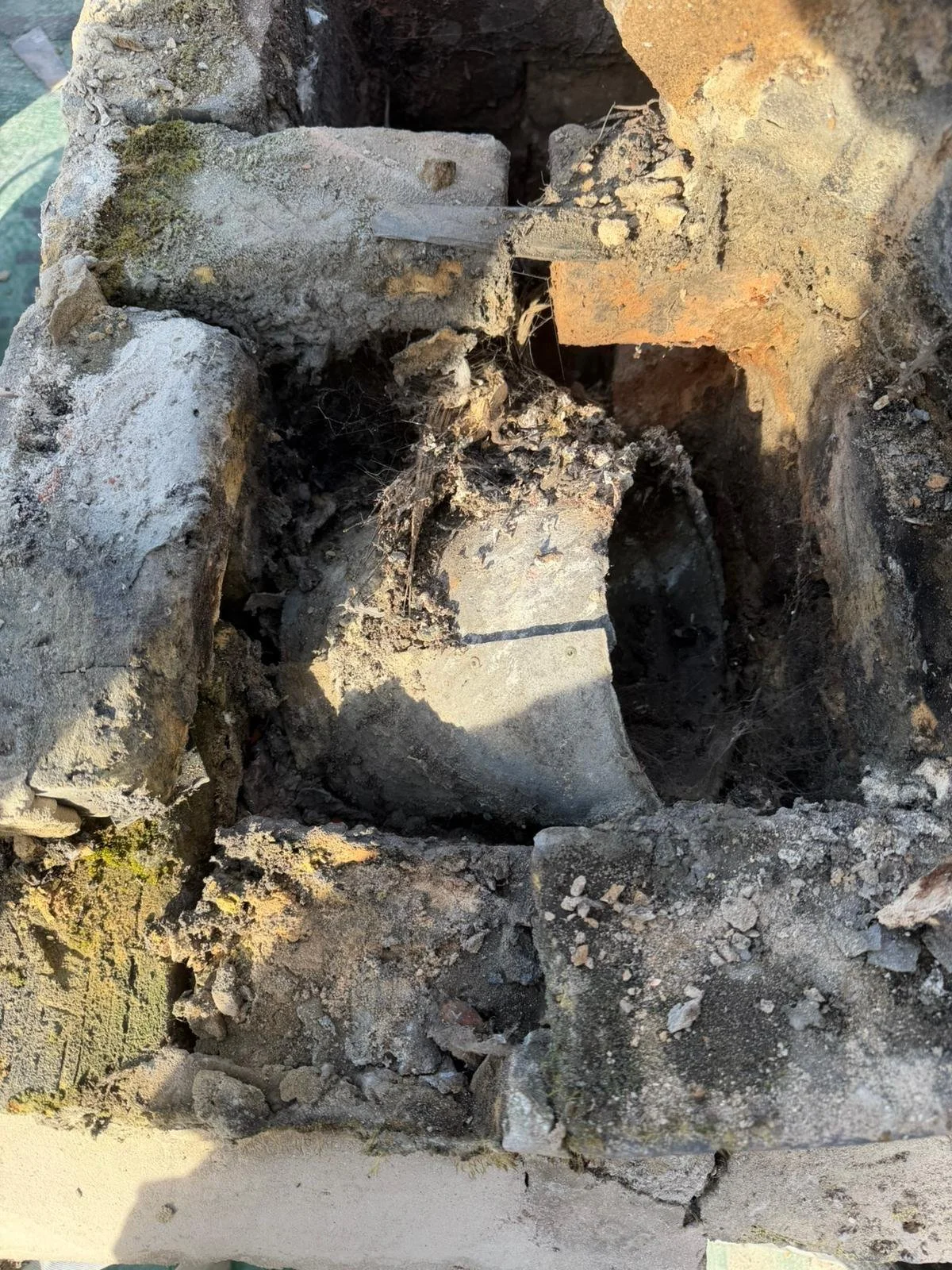 Close-up of broken and weathered concrete and bricks with dirt and debris inside a damaged wall or structure.