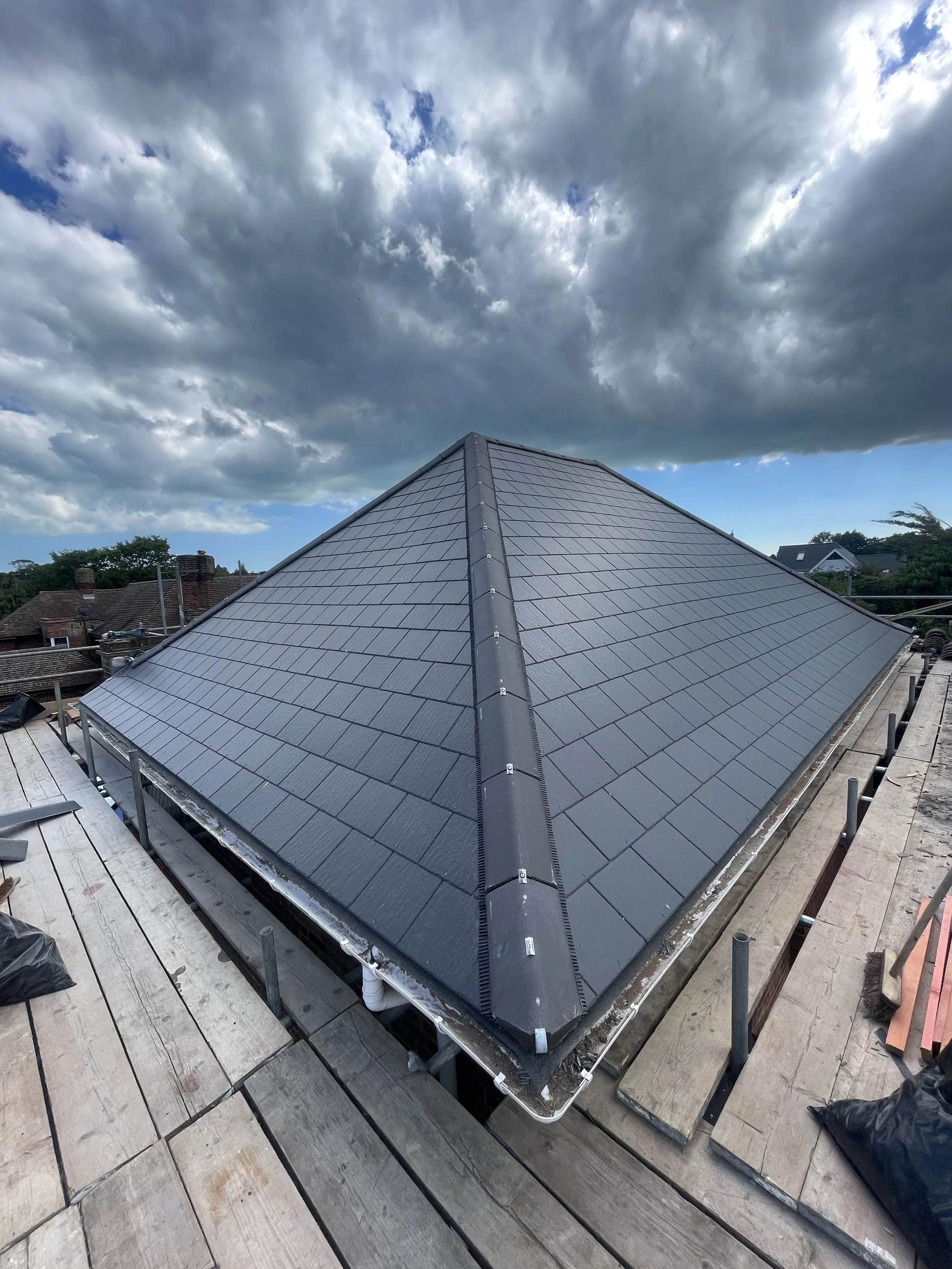 Newly installed dark gray slate roof on a house with a steep pitch, seen from the rooftop under cloudy skies.