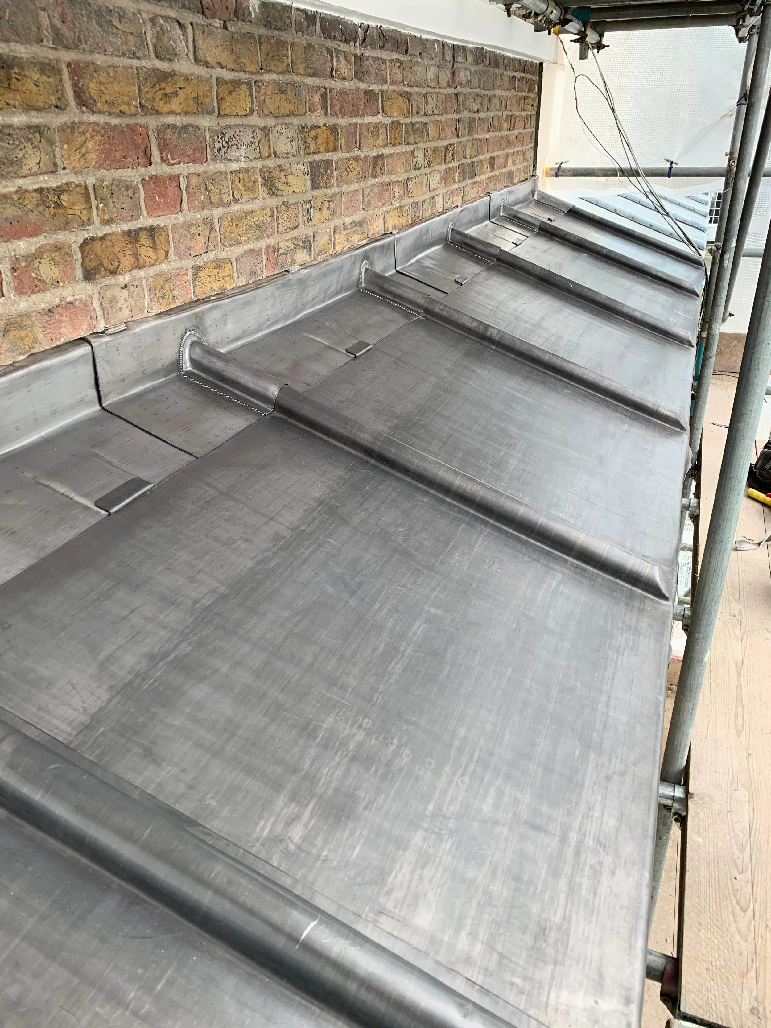 Freshly installed metal roof panels on a building with a brick wall and construction scaffolding.