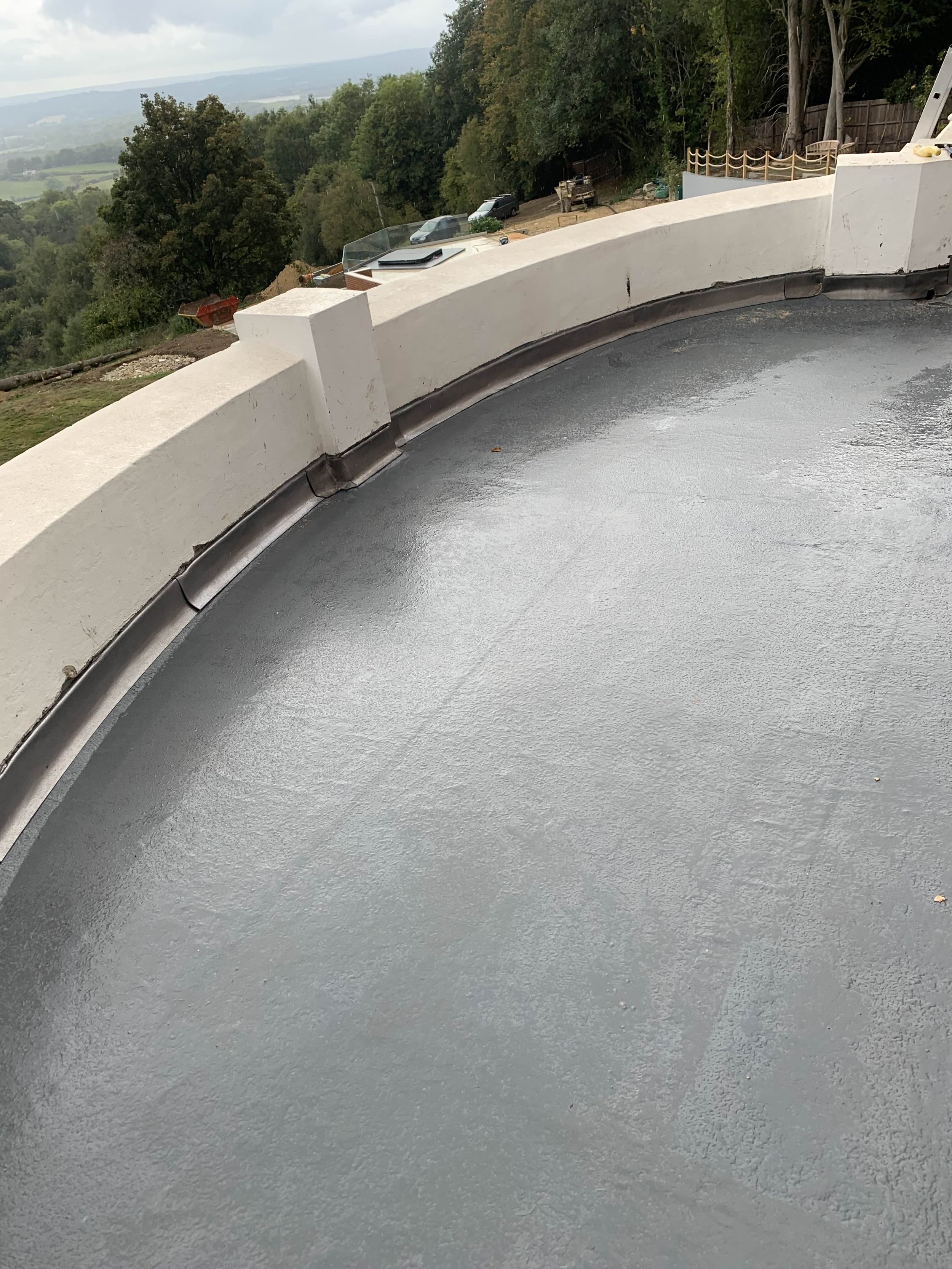 Close-up of a rooftop with a gray waterproof coating, white concrete parapet wall, and metal flashing around the edge.