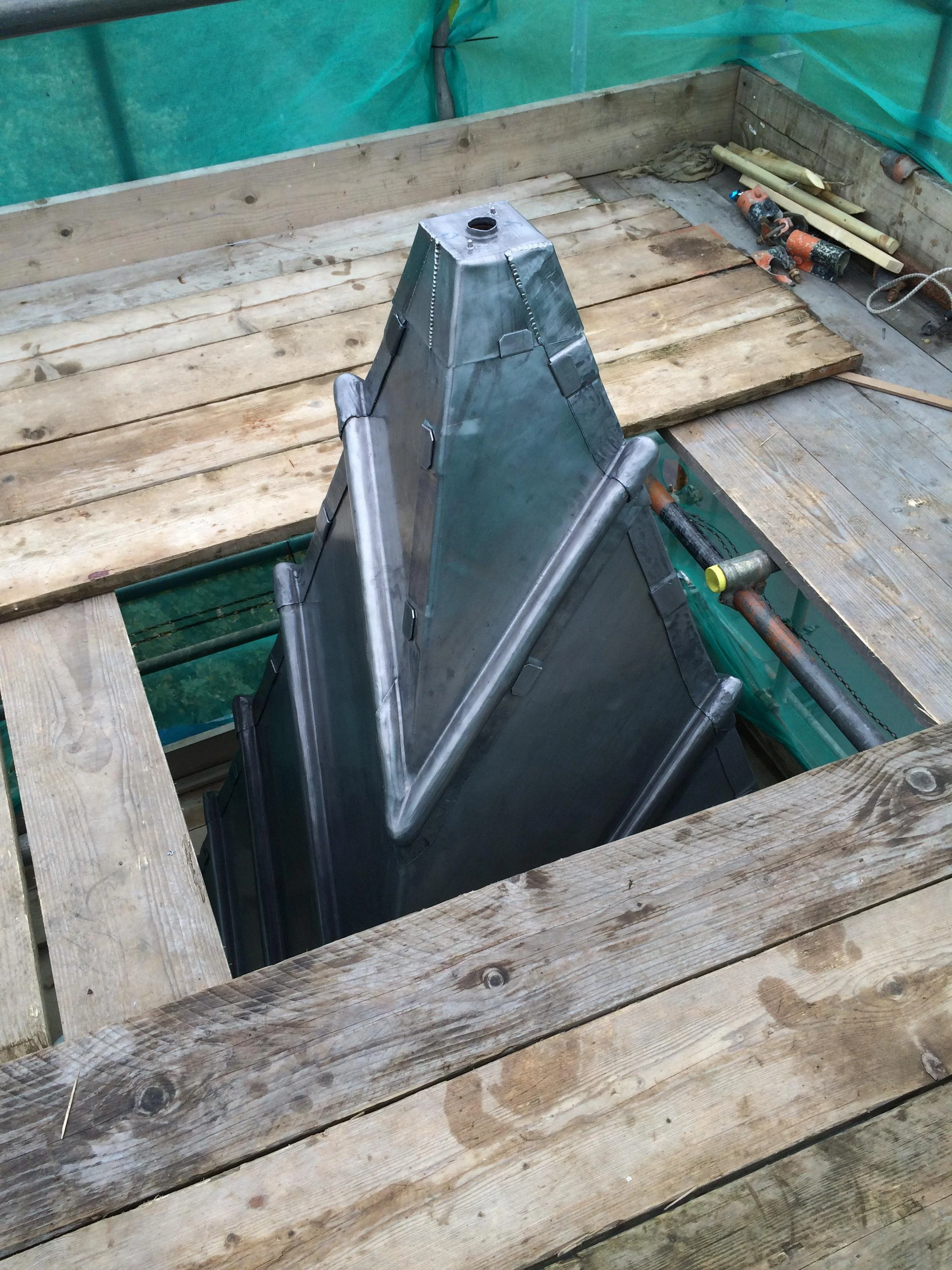 A metal structure with a pyramid shape under construction inside a wooden framework, with tools and wooden planks around.