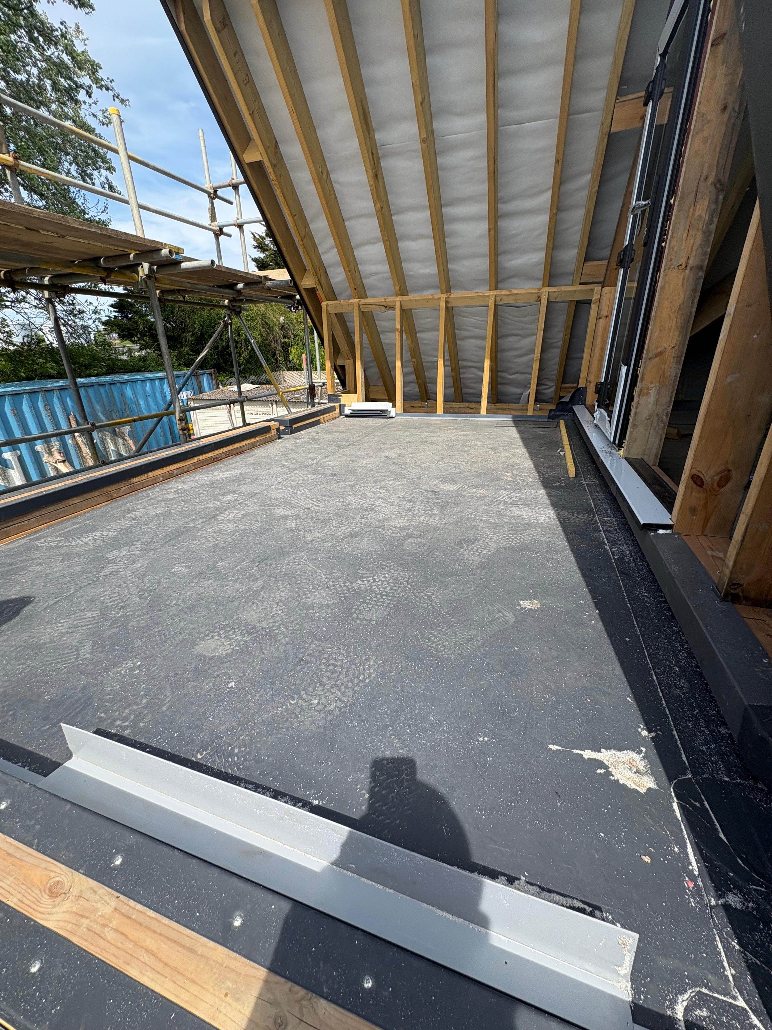 Construction site of a new balcony with unfinished wooden framing and a concrete floor, surrounded by scaffolding.