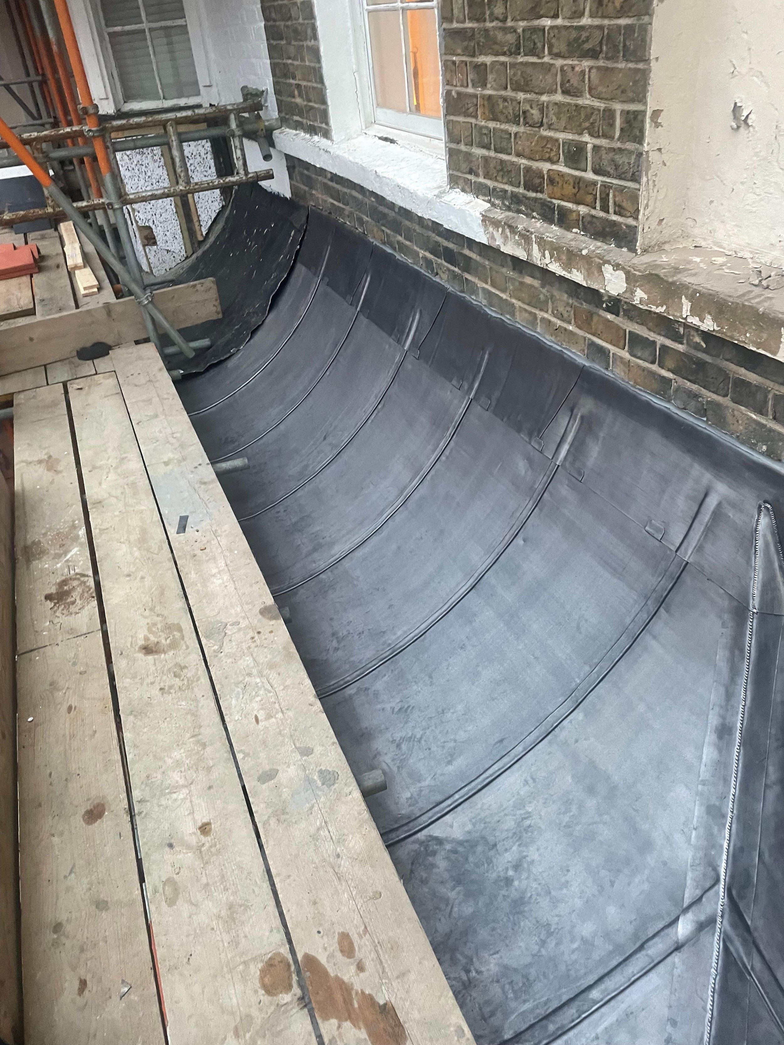 Construction site showing a sloped roof with a waterproof membrane, scaffolding, and brick walls of a building.