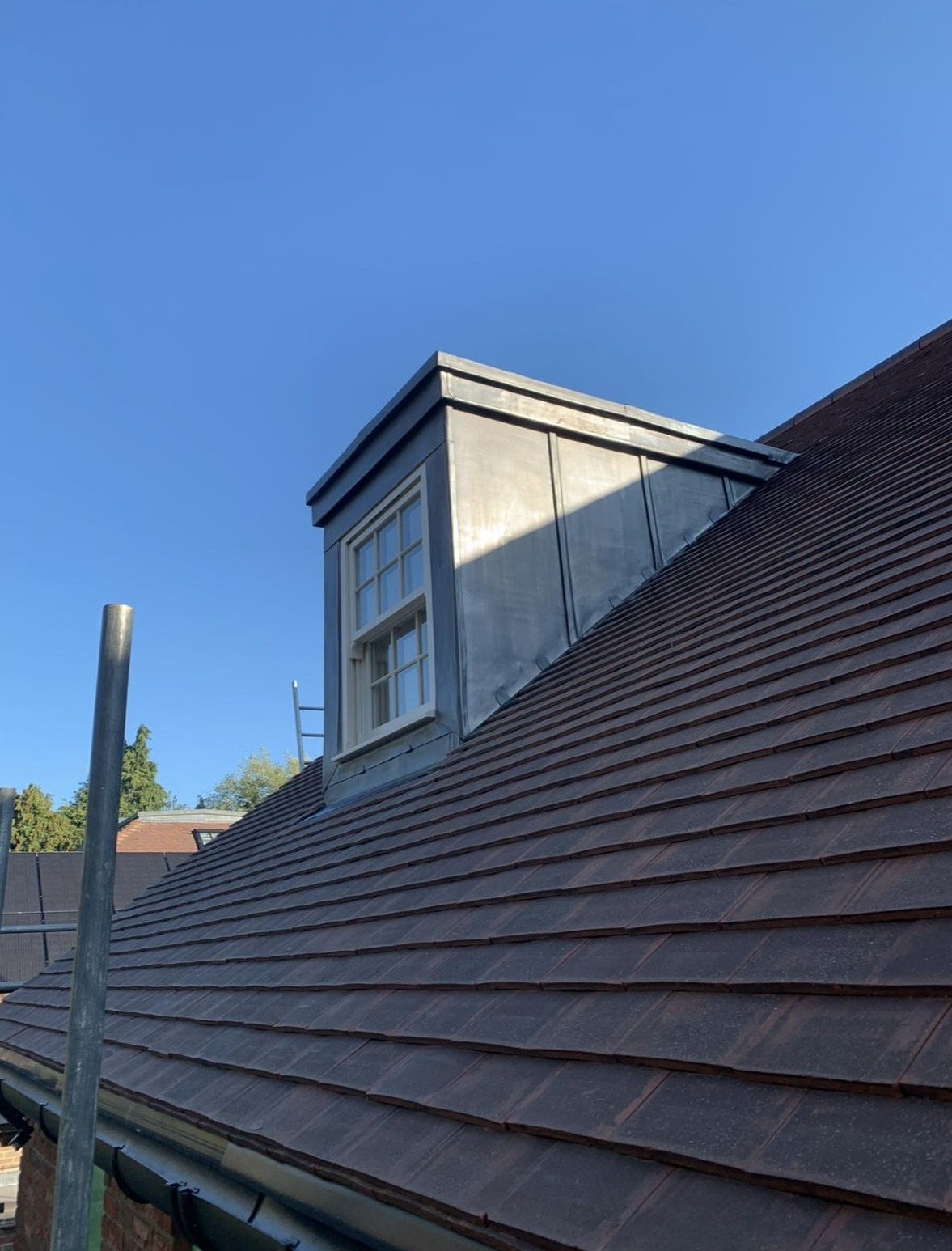 View of a rooftop with red tiles, a dormer window protruding from the roof, and a clear blue sky in the background.