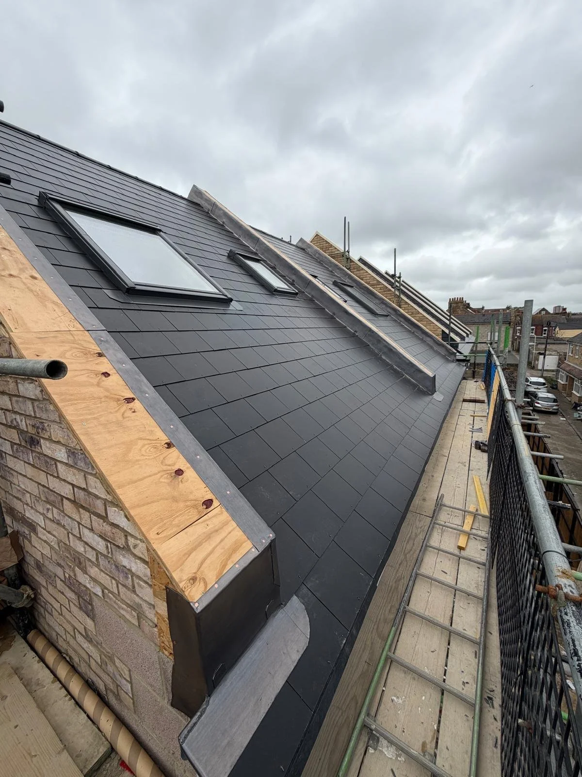 Roof with black shingles, skylights, and construction scaffolding on the sides under cloudy sky.