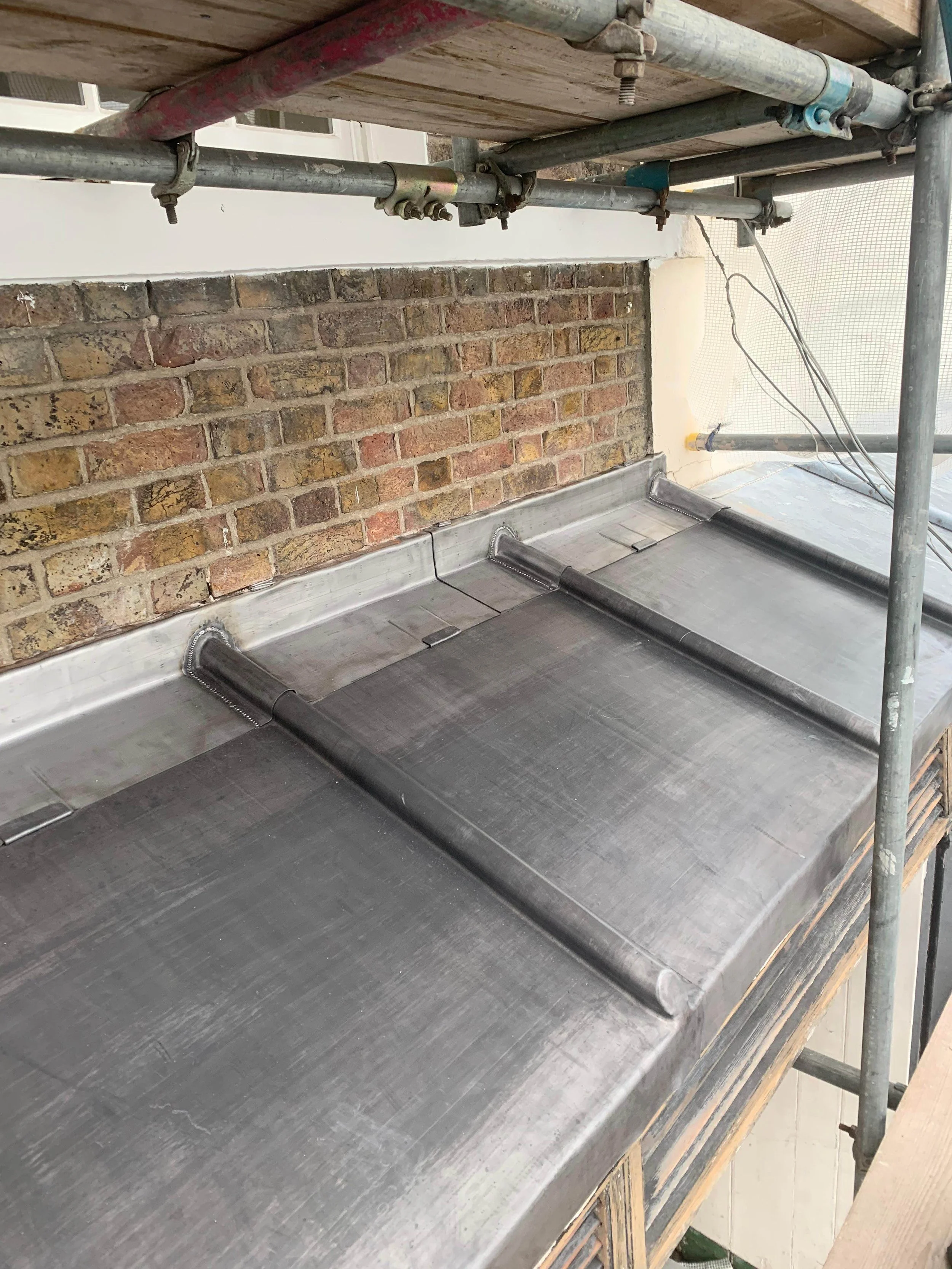 Metal roofing panels installed on a building under construction, with brick wall in the background and scaffolding around the area.