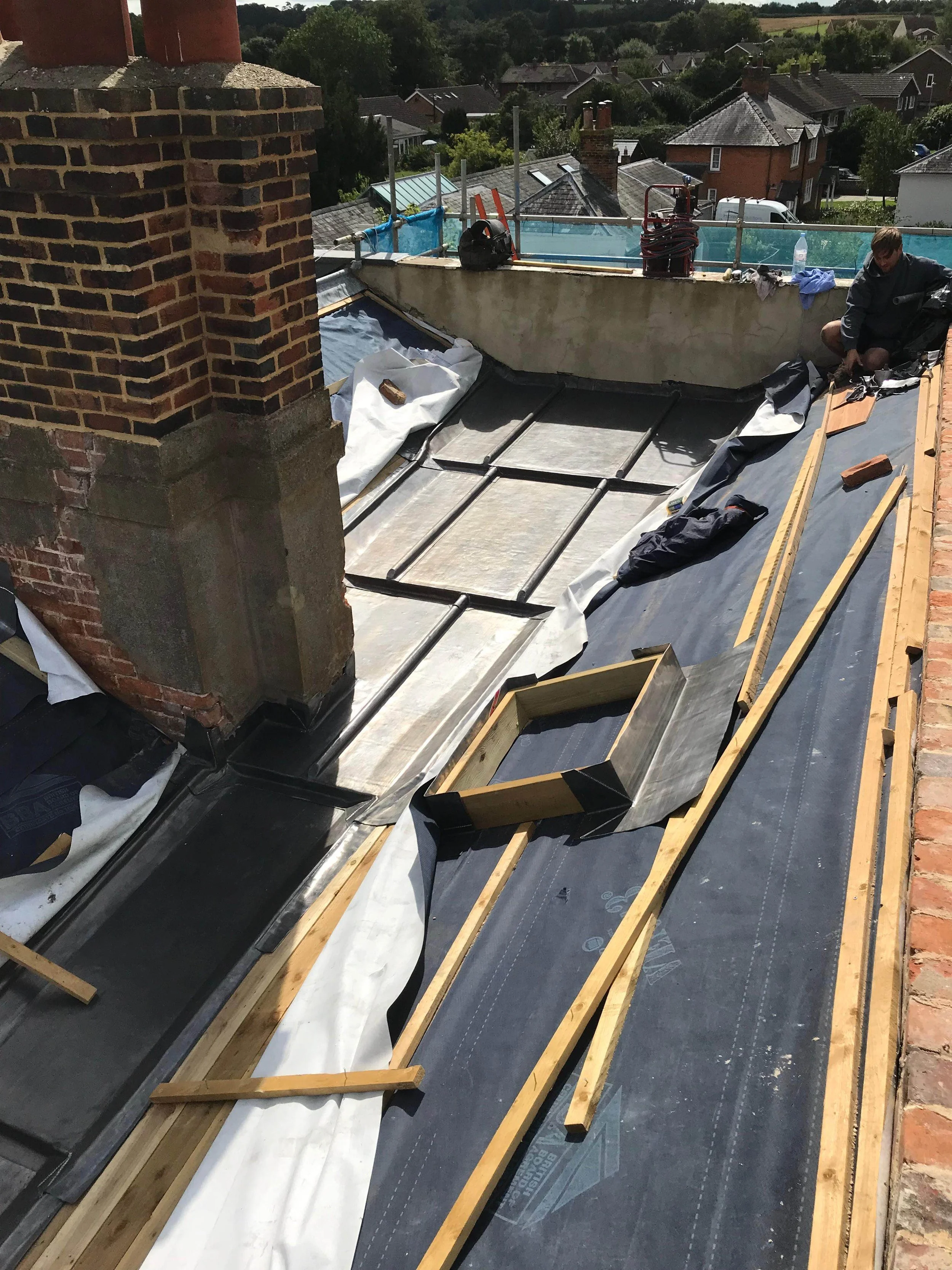 Rooftop under construction with wooden framework, black roofing material, and a worker installing or inspecting the roofing on a residential building.