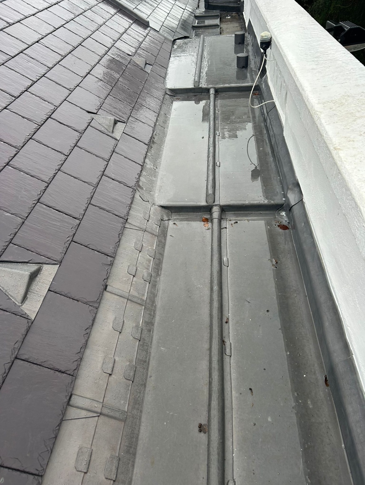 Roof with gray shingle tiles and newly installed metal flashing around the edge.