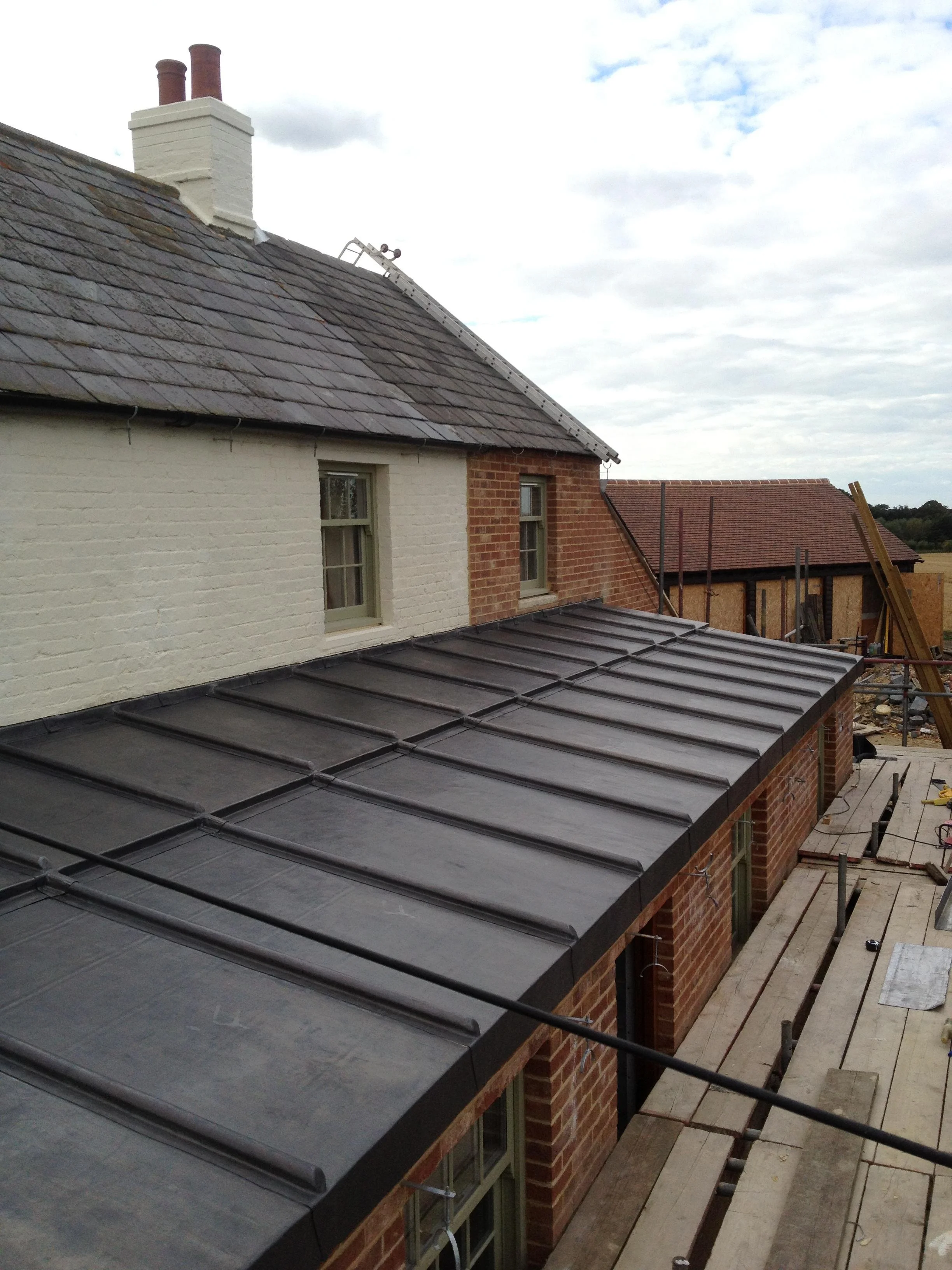 Construction site with a building featuring brick walls, new metal roofing, and scaffolding.