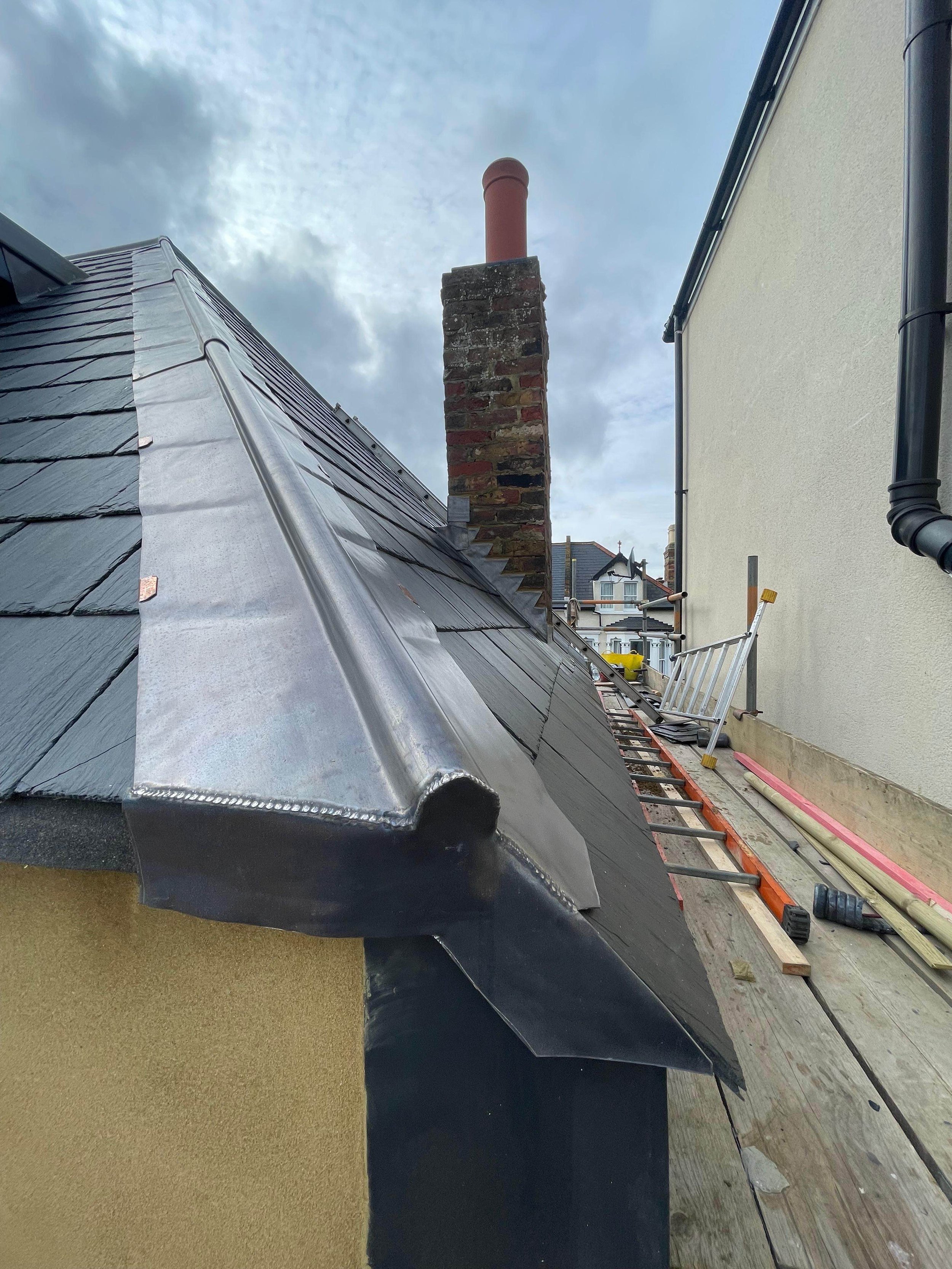 Upgraded roof with new dark metal roofing, a brick chimney, and a street view in the background.