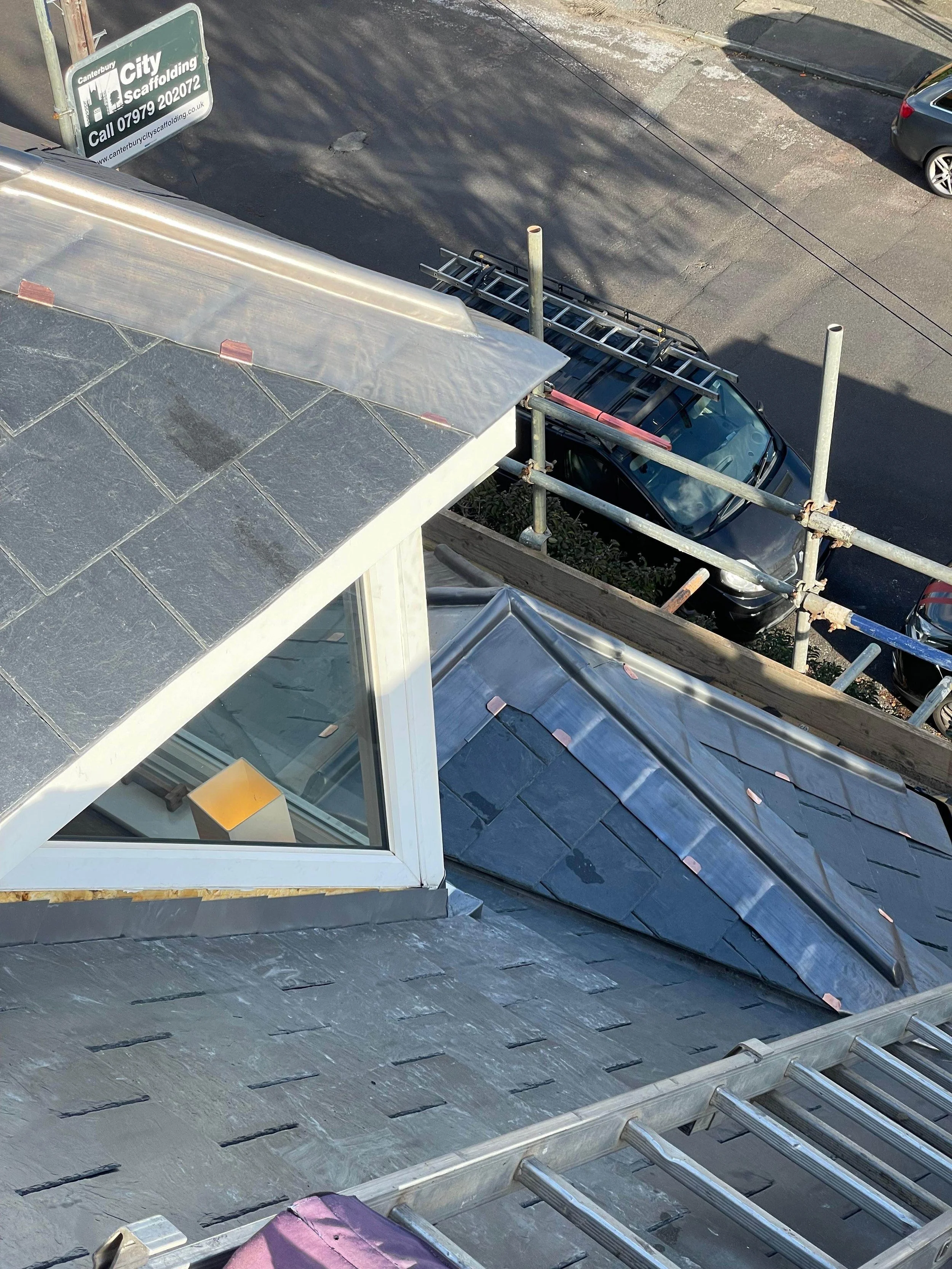 View from a building roof looking down at a street with parked cars, scaffolding, and a sign for Canterbury City scaffolding.