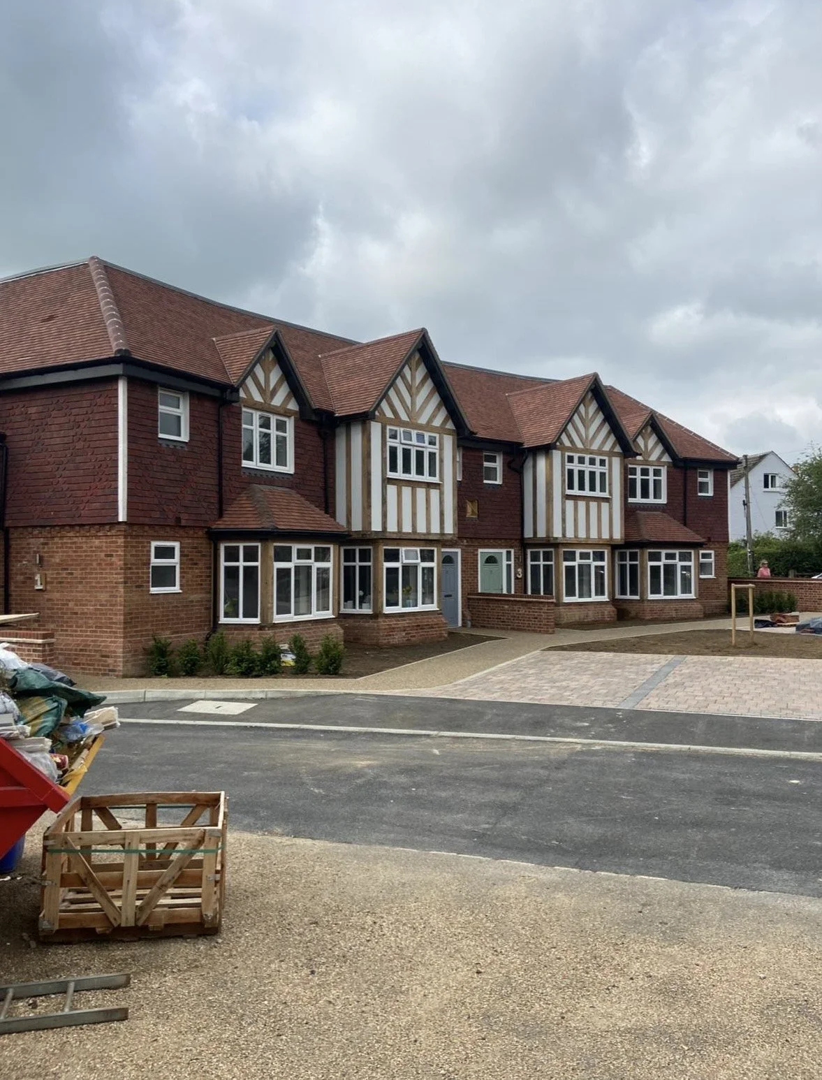Newly constructed multi-story residential buildings with brick and half-timbered decorative exteriors and pitched roofs, under a cloudy sky.