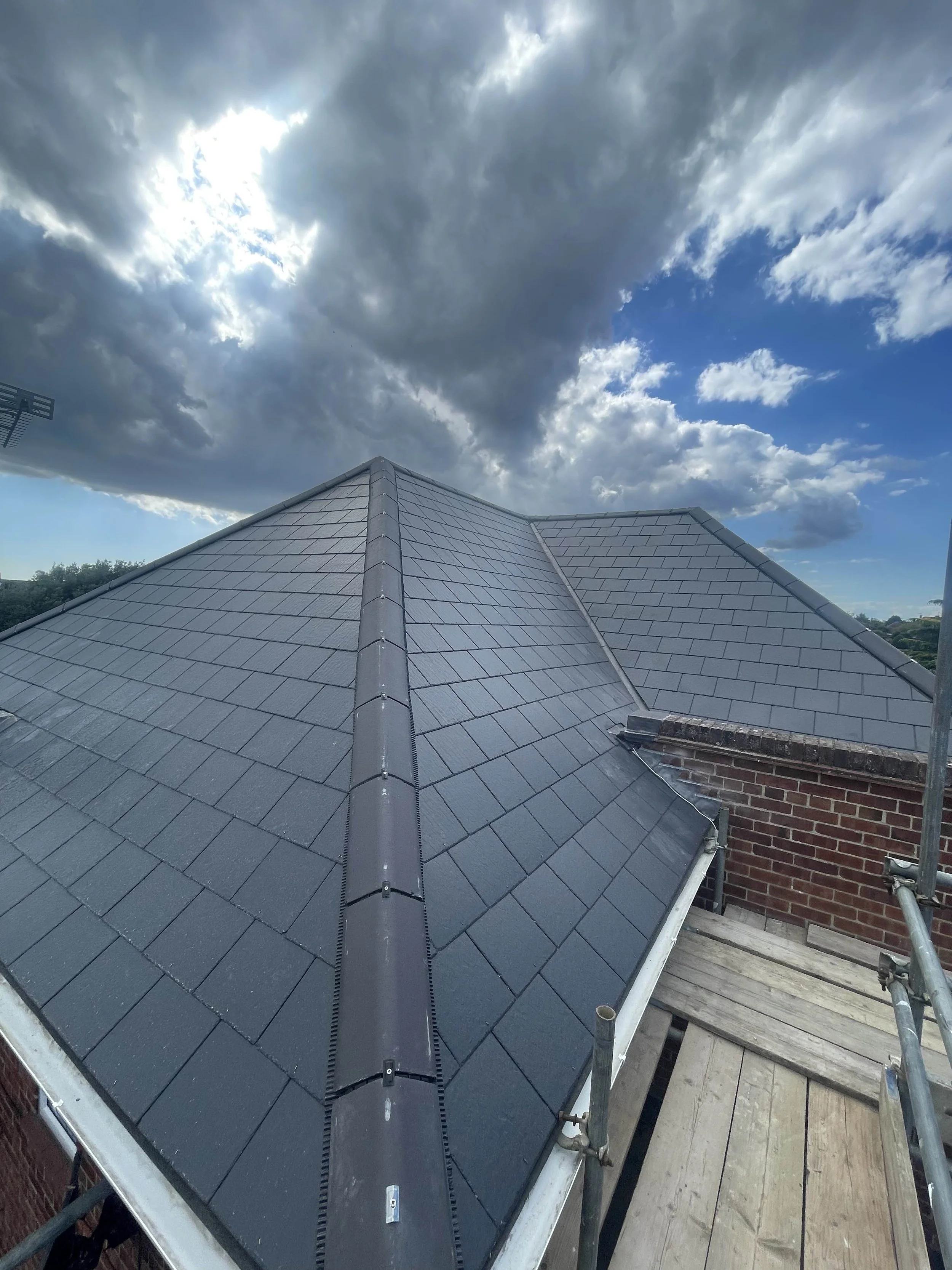 A gray tiled roof under a partly cloudy sky with dark and white clouds.