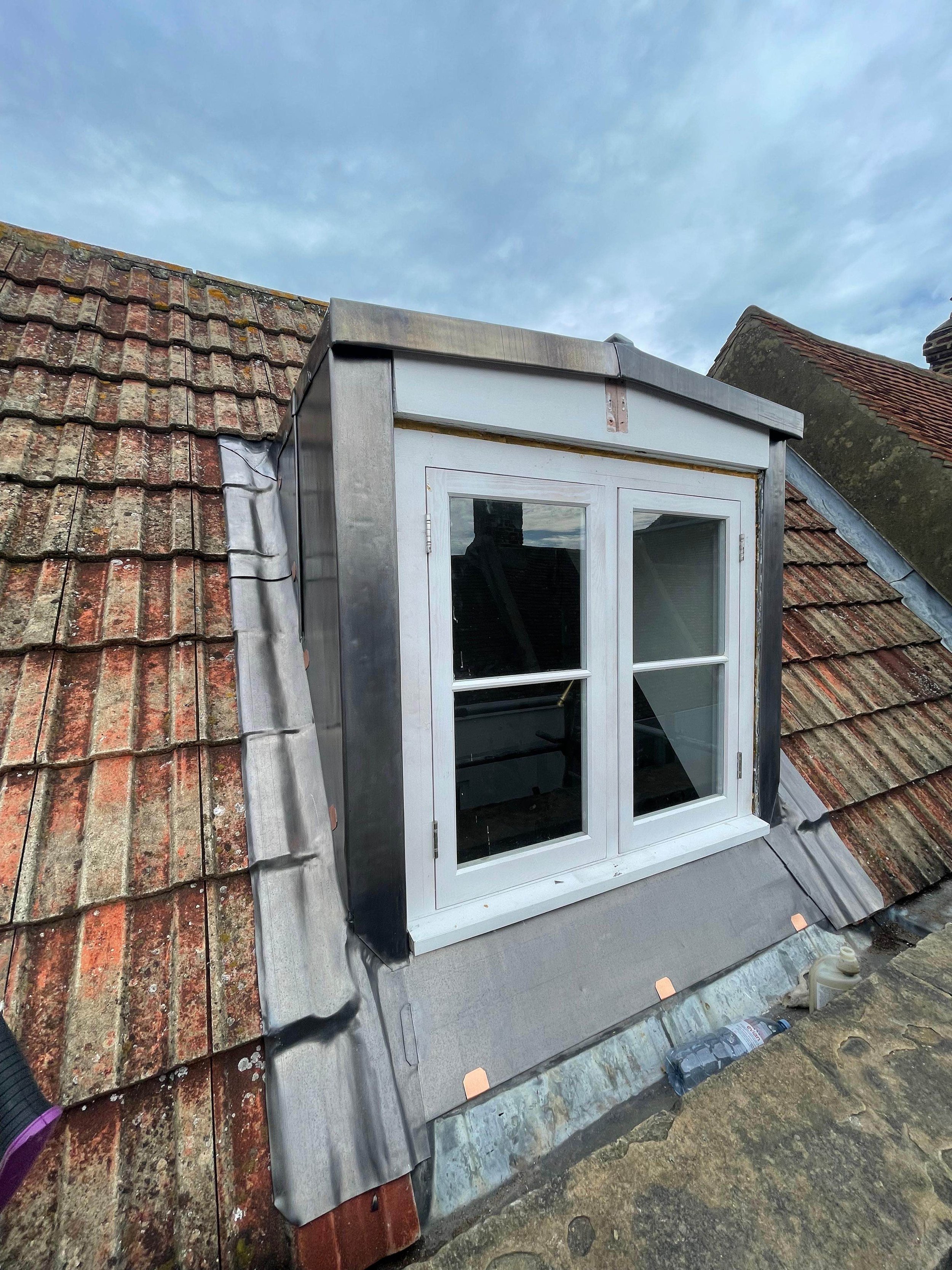 Construction work on a dormer window on a tiled roof, with construction materials and tools nearby.