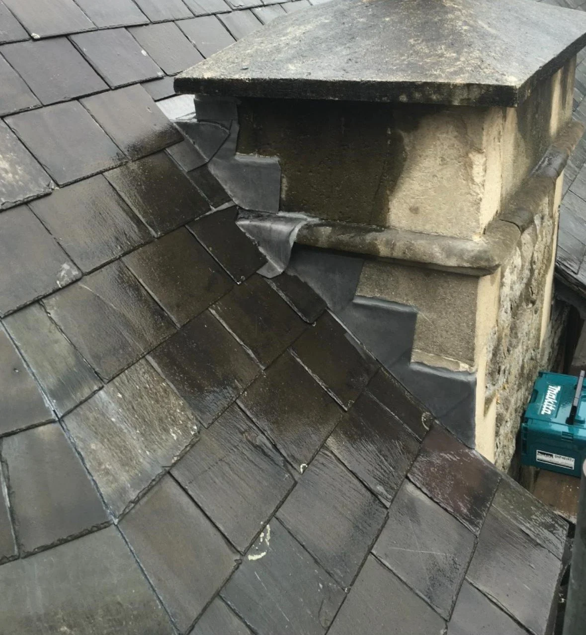 Close-up of a chimney with black slate roof tiles, showing recently repaired flashing around the chimney.