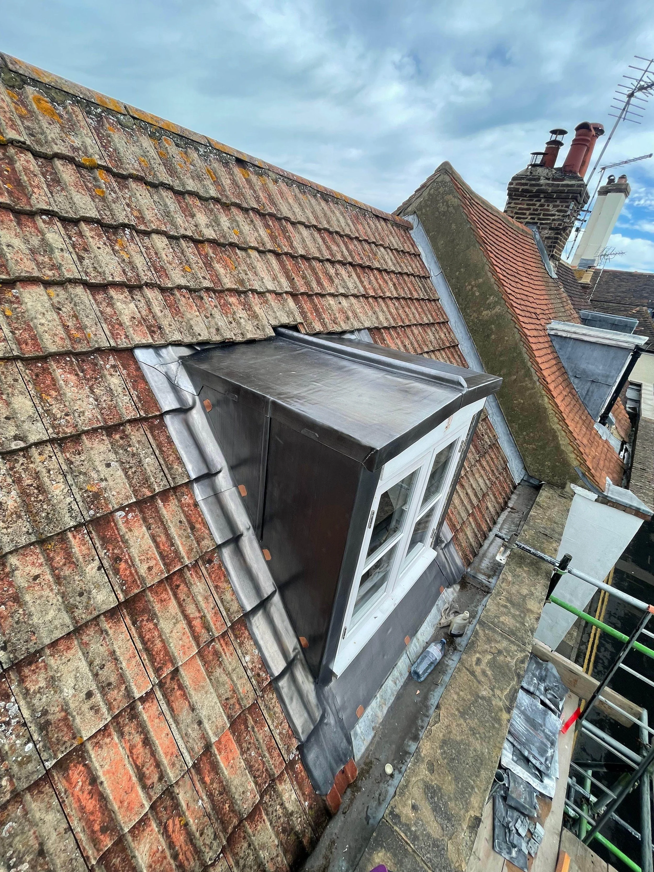Roof with old and new roofing materials, including a skylight window, scaffolding, and construction tools.