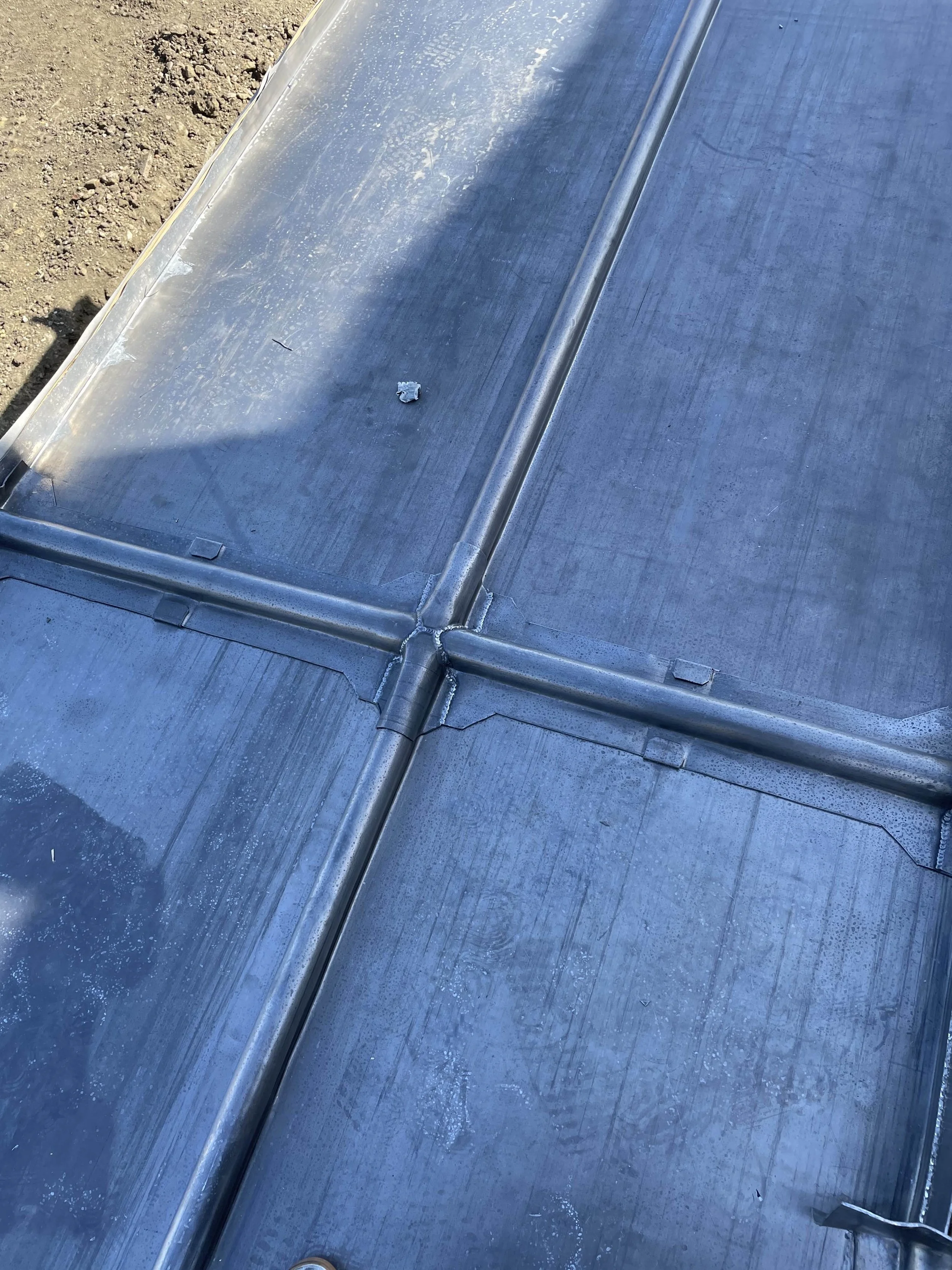 Close-up view of a metal roof with visible seams, joints, and some dirt and debris on the surface.
