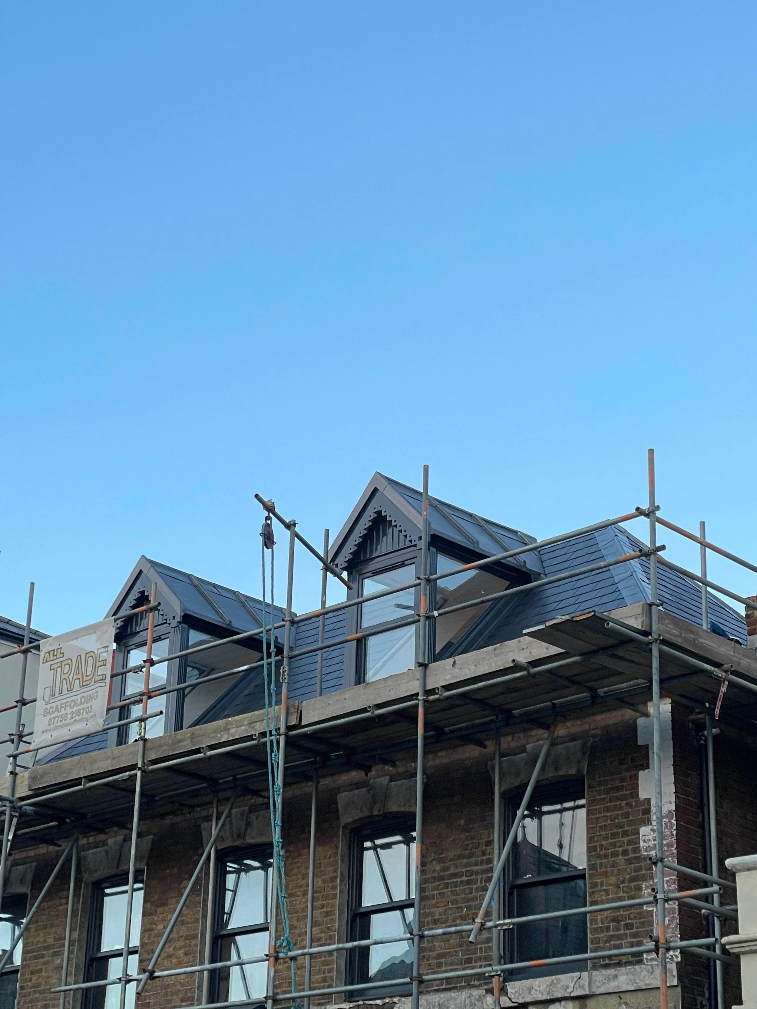 Building under construction with scaffolding, brick exterior, and dormer windows on the roof.