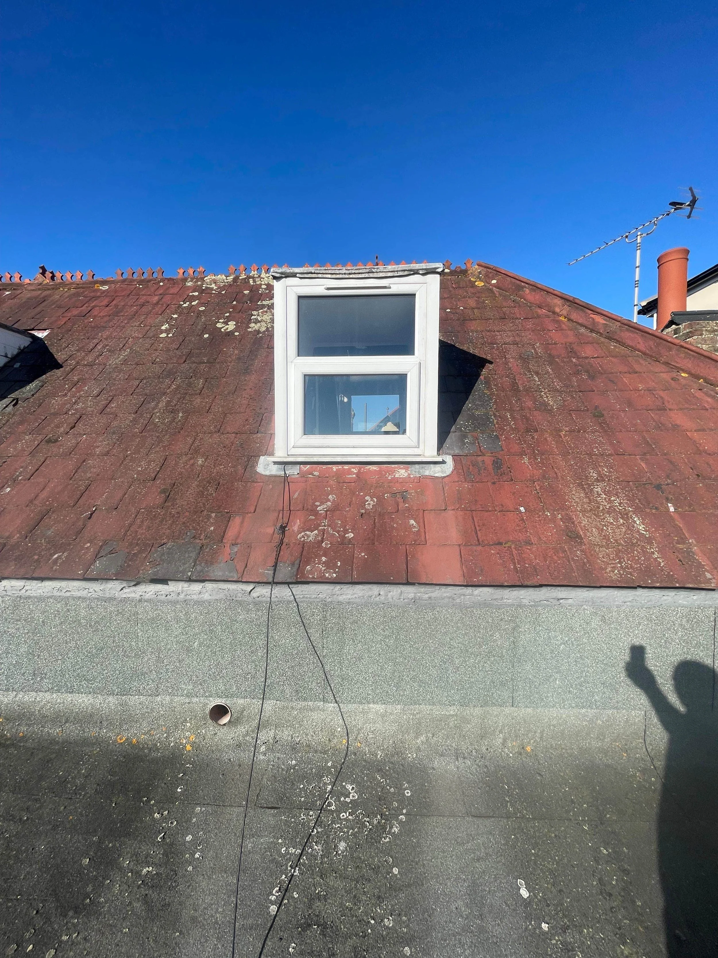 Roof with aged red shingles, white-framed dormer window, and a blue sky.