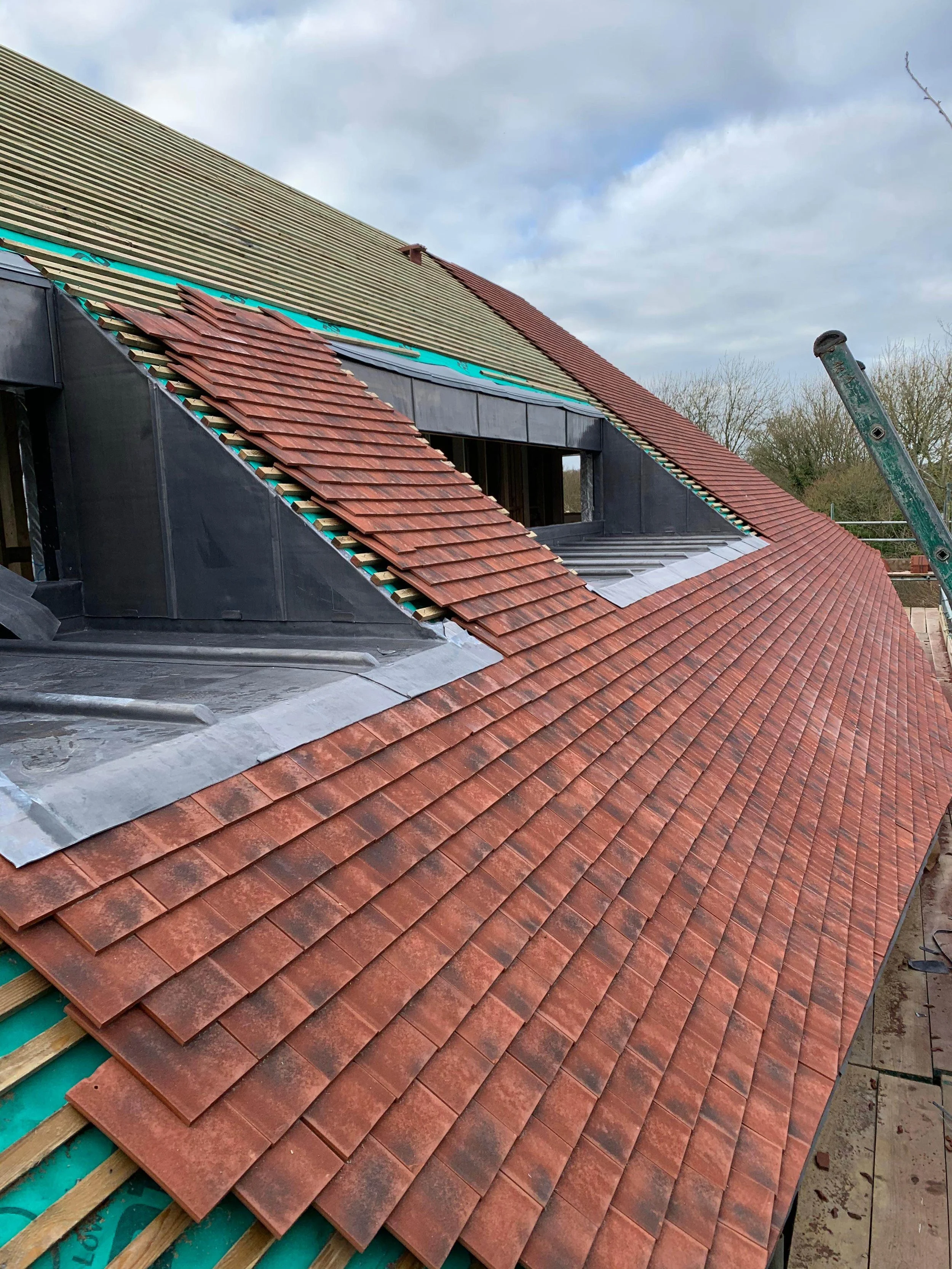 Construction of a sloped roof with new reddish-brown roof tiles, under partial sky with some clouds.