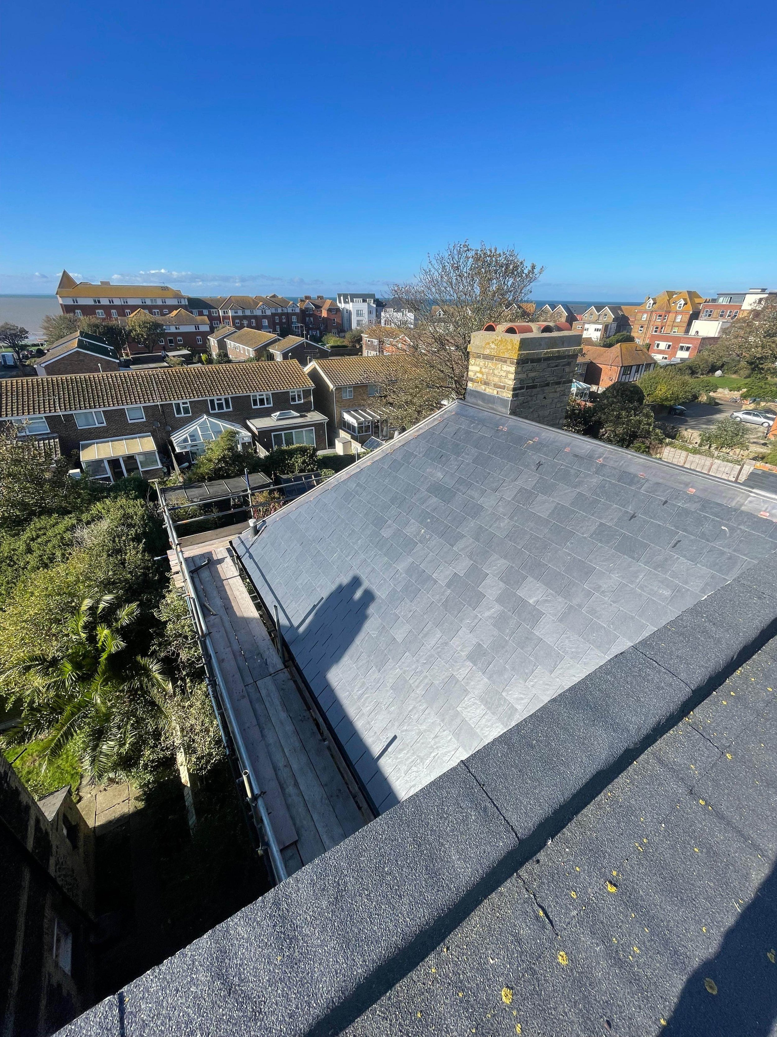A rooftop view overlooking a residential neighborhood with trees, houses, and a clear blue sky.