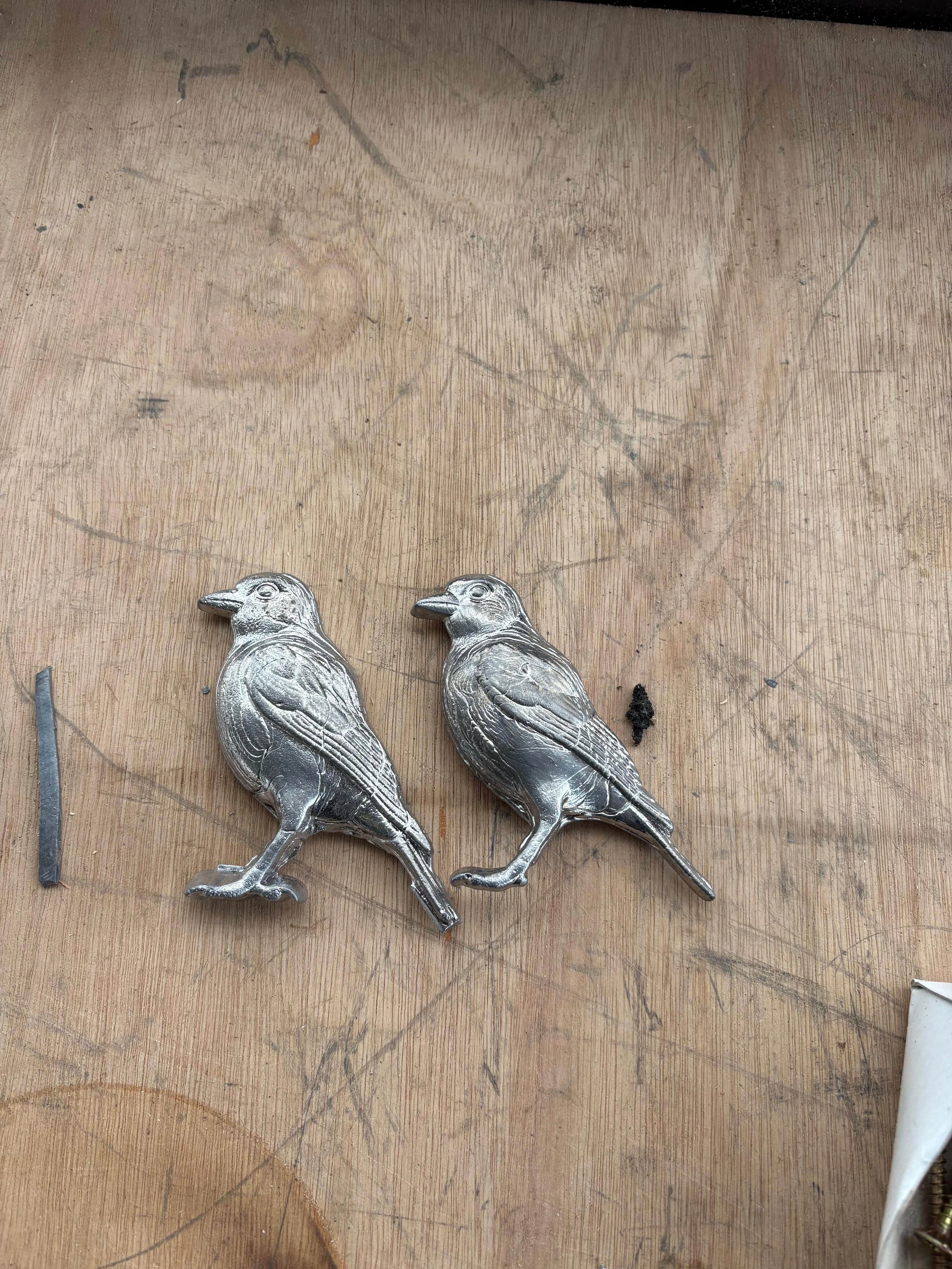 Two metal bird-shaped emblems placed on a wooden surface.