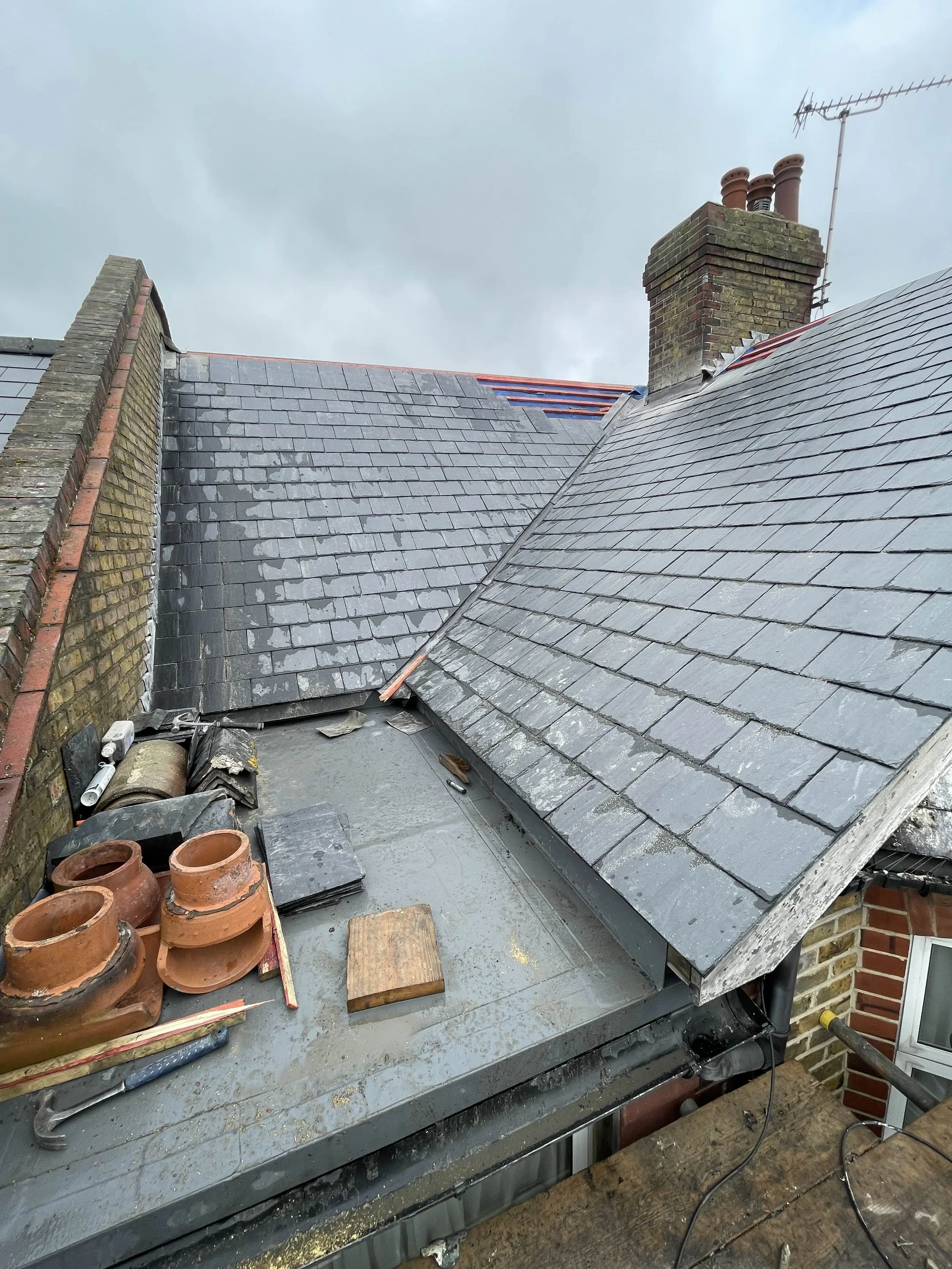 Rooftop with new slate roofing tiles and several clay chimney pots. Overcast sky in background.