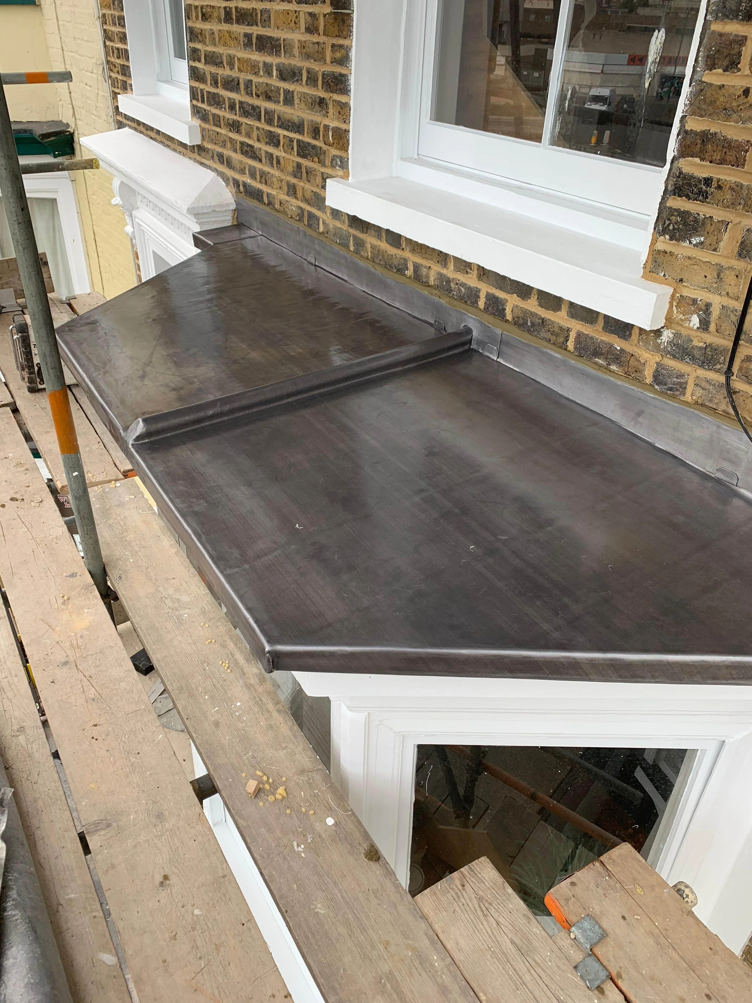Metal window sill on a brick wall with a construction scaffold and a window.