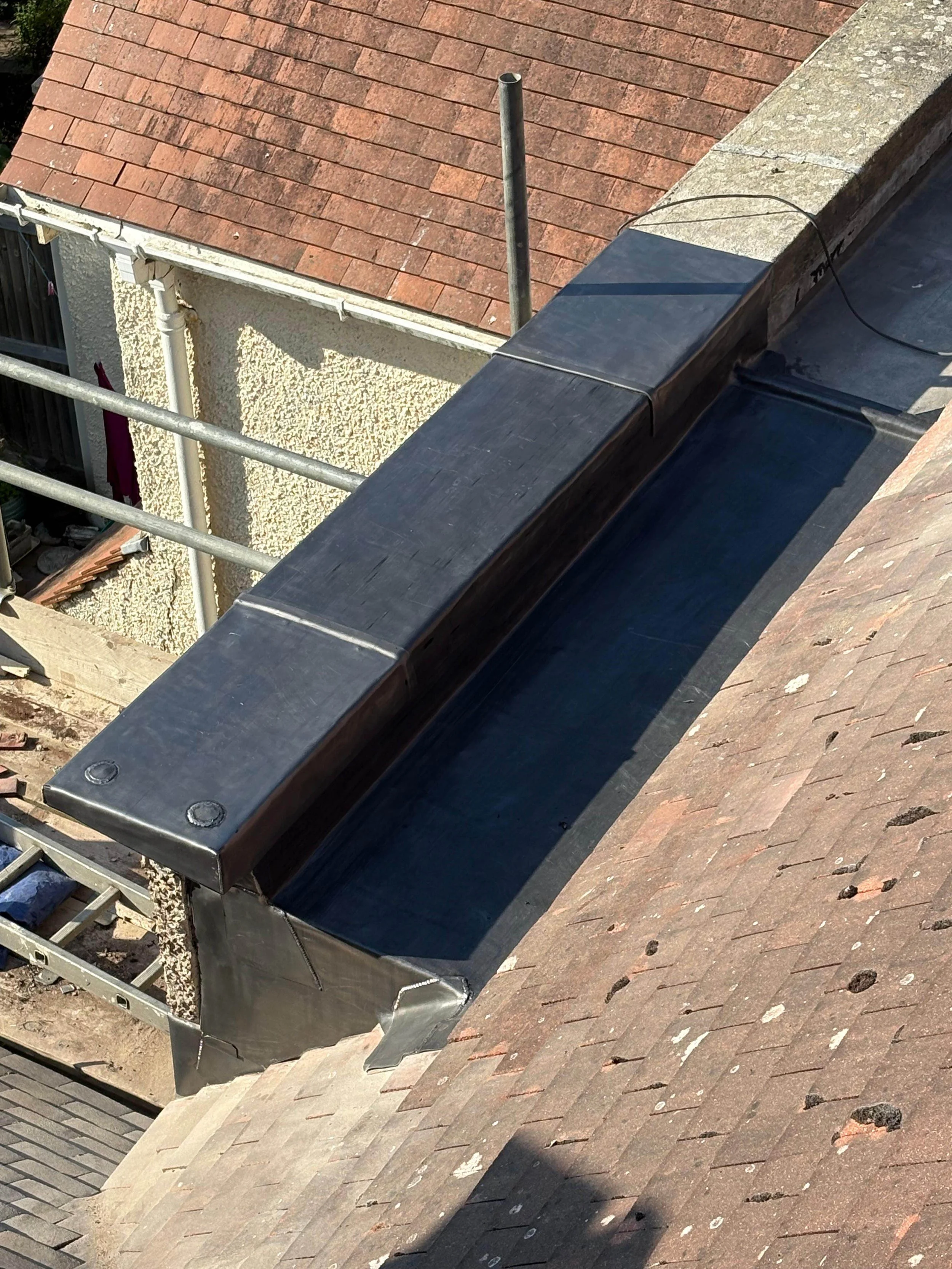 View of a roof with a black metal chimney flashing surrounded by shingle roofs and scaffolding.