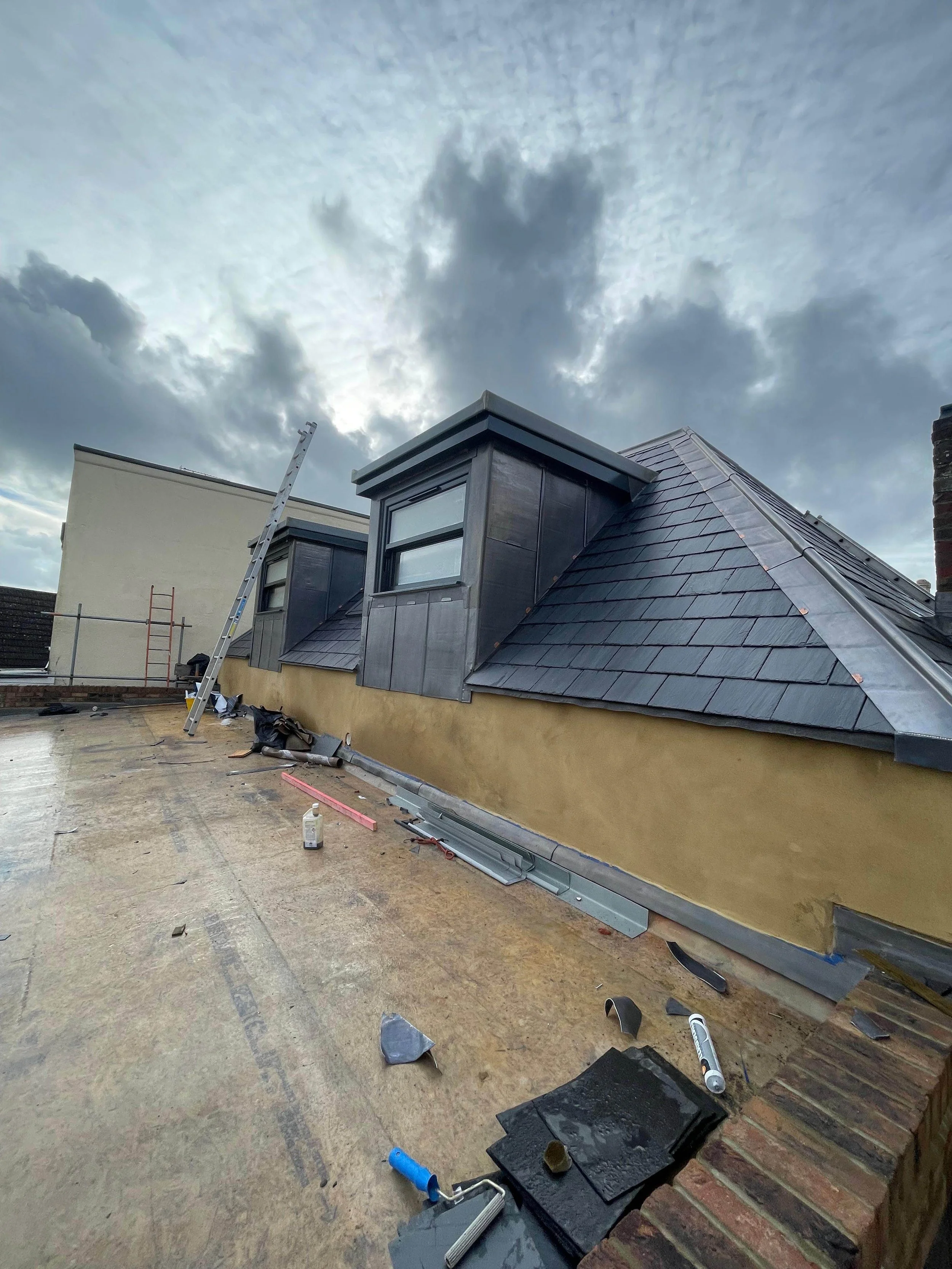 Rooftop under construction with tools and materials scattered, cloudy sky overhead.