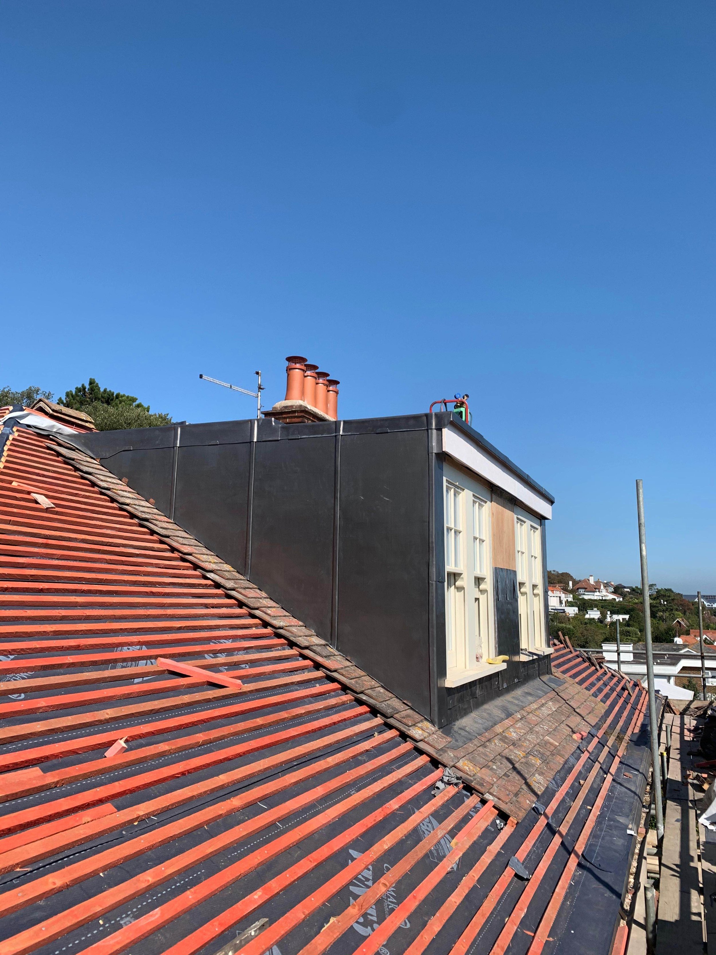 Roof with red tiles under construction, with new underlayment visible, against a clear blue sky.