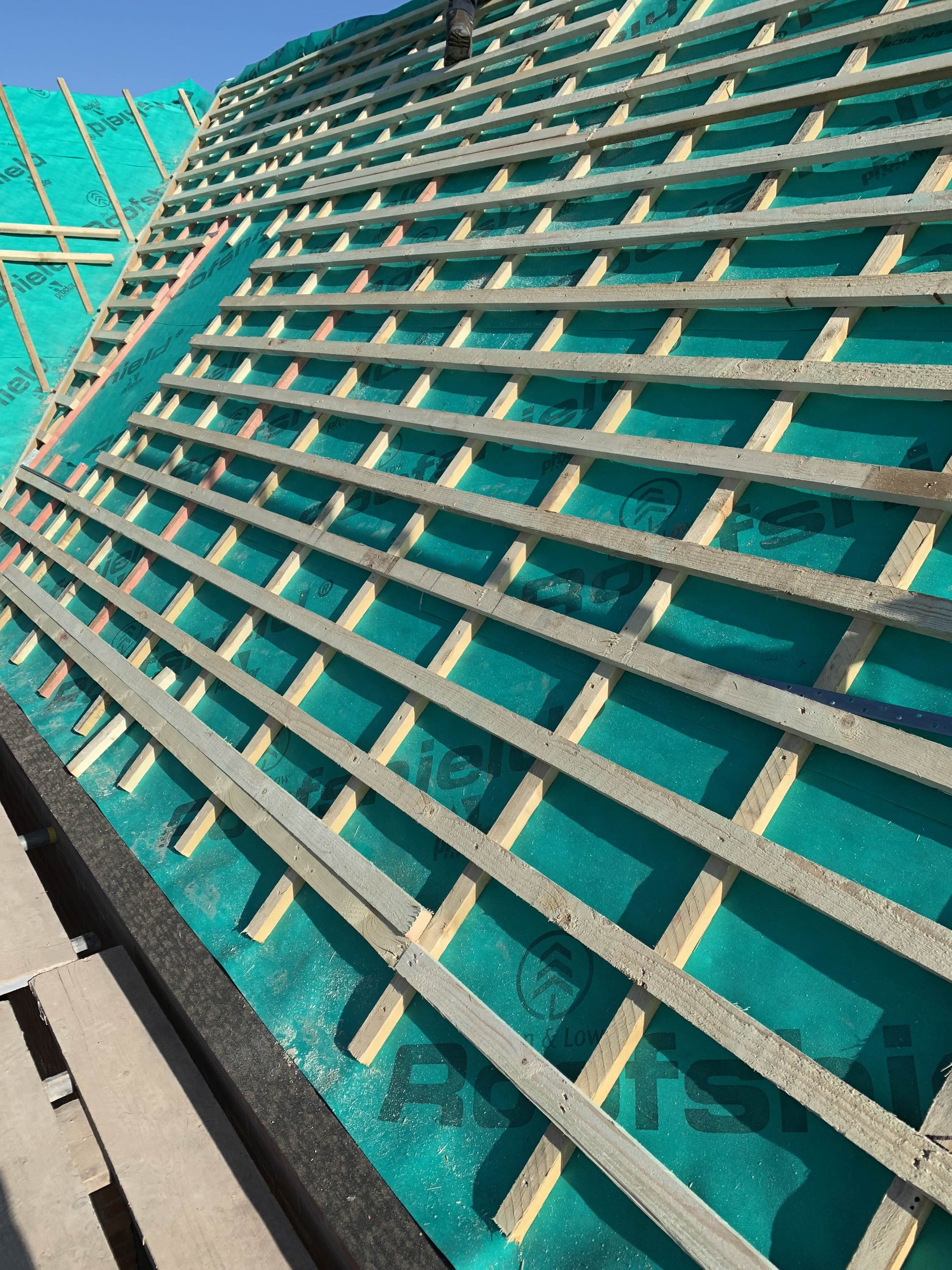 Construction site with wooden and metal framework on a roof under clear blue sky.