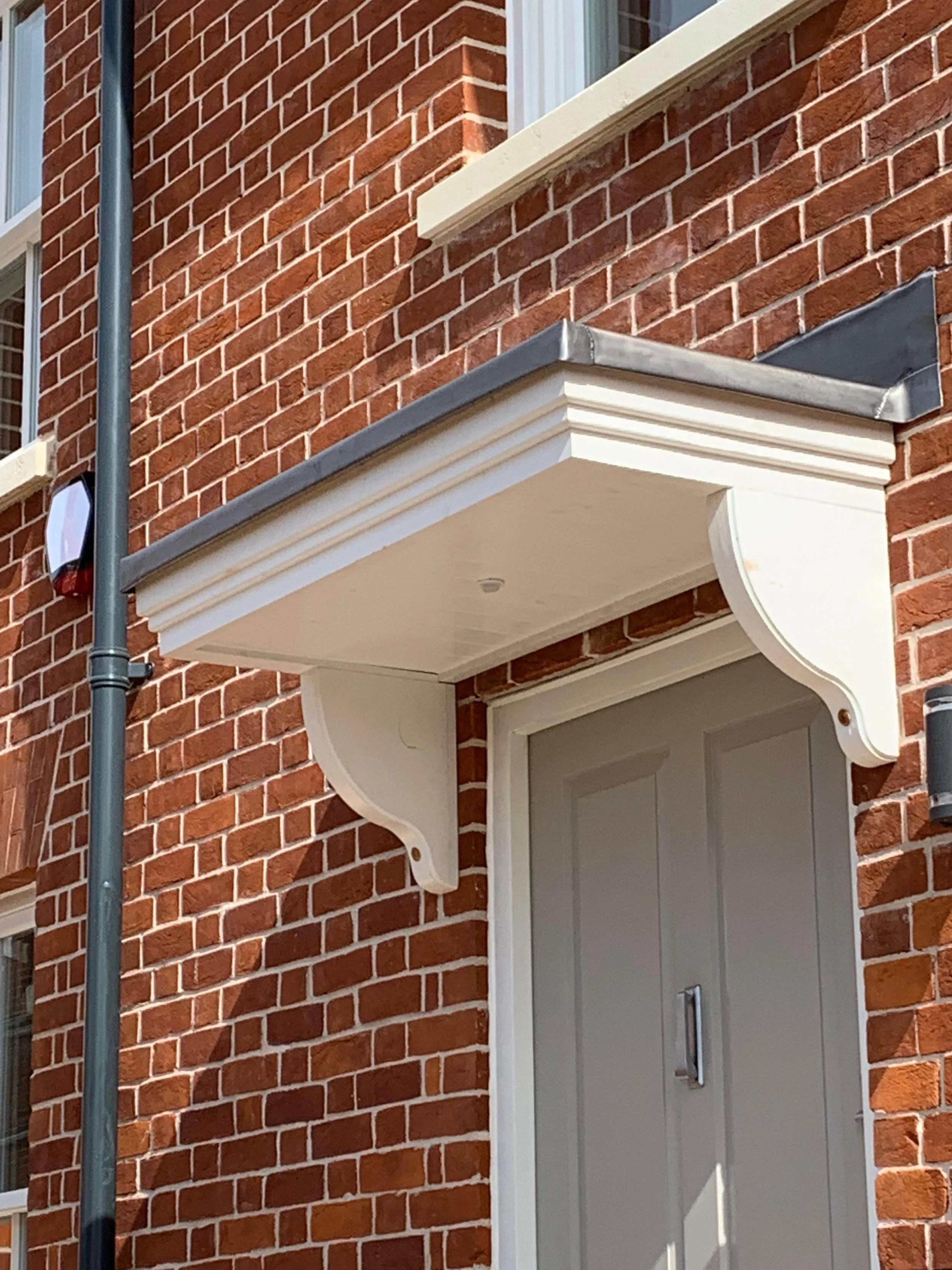Close-up of a brick building exterior showing a white decorative door canopy supported by white brackets, over a grey door.