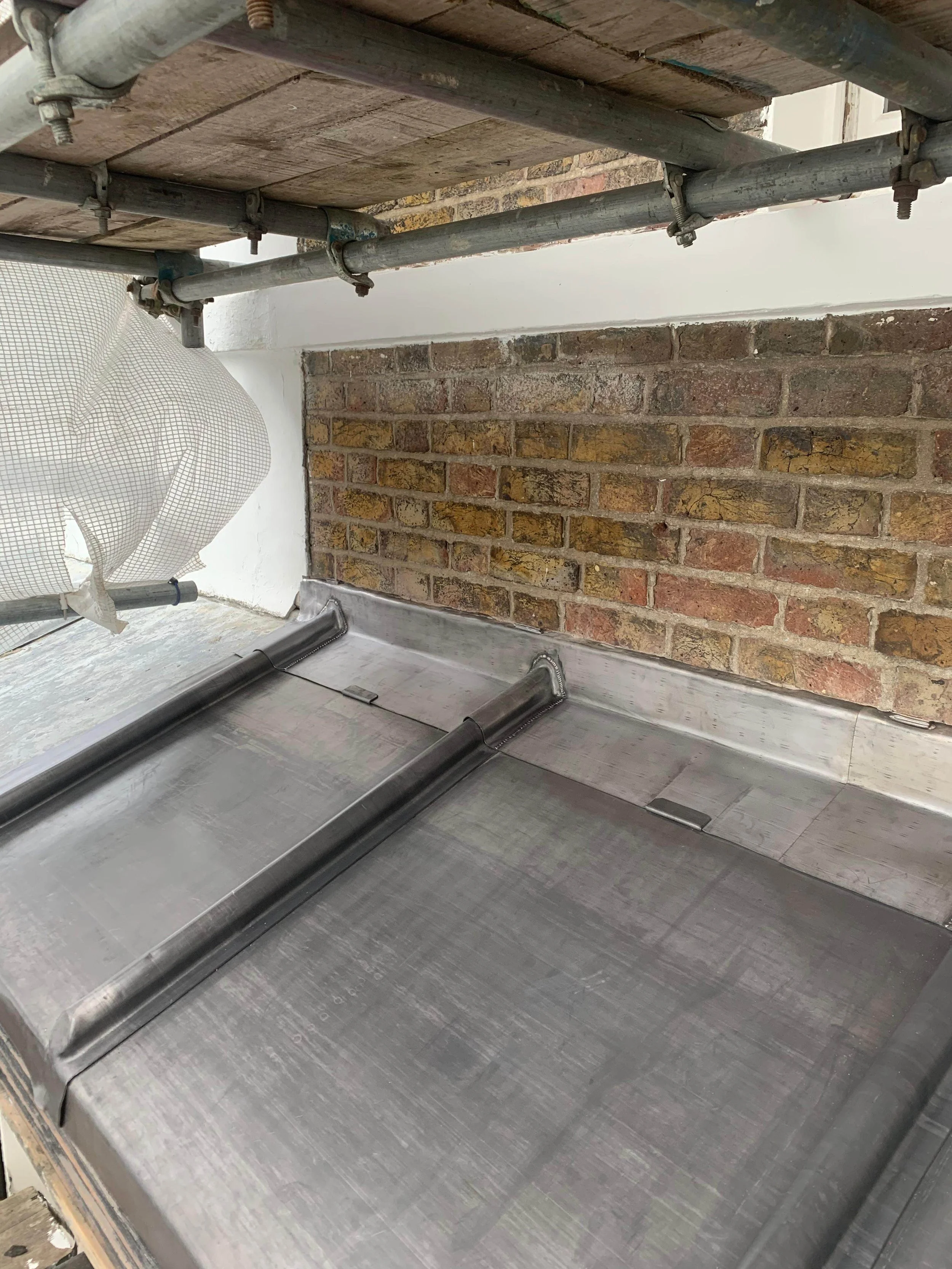 Close-up of a metal roof flashing installation with a brick chimney and scaffolding.