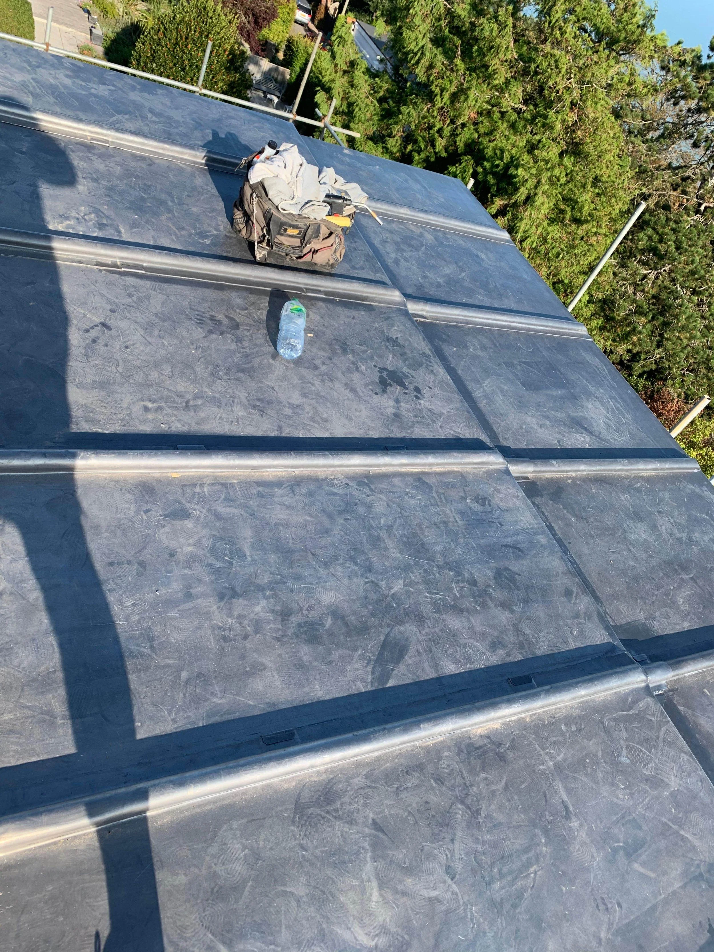 View of a rooftop with tools and a water bottle placed on it, with greenery and trees in the background.