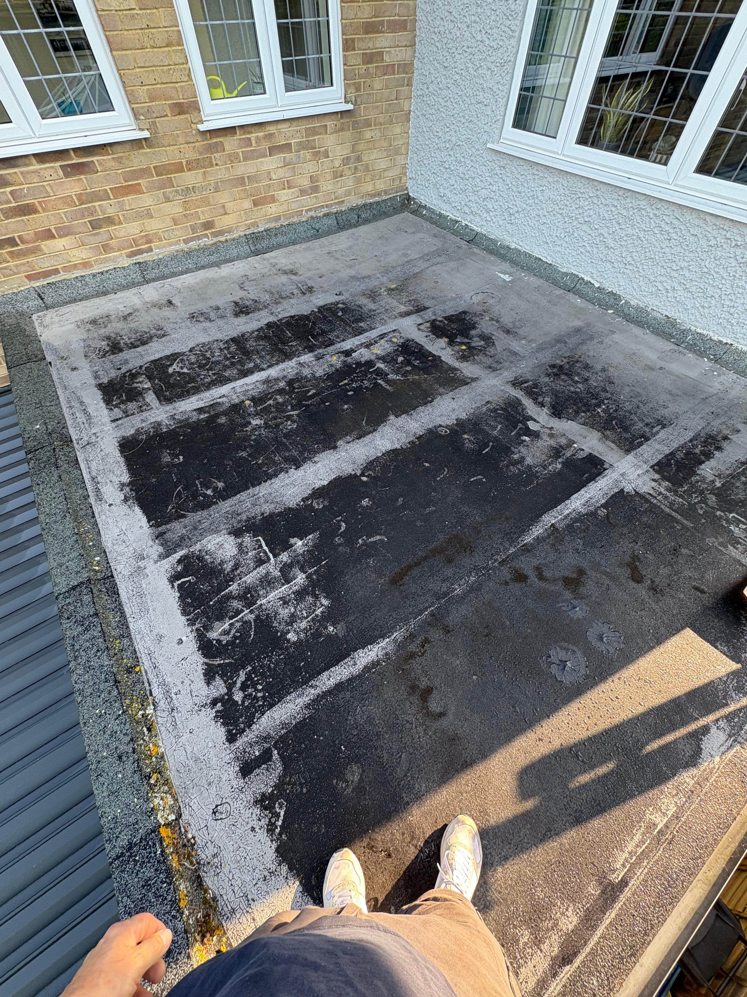 A rooftop balcony with a worn, partially stripped black surface, white paint markings, and patches of dirt, with the person's feet visible at the bottom of the image.
