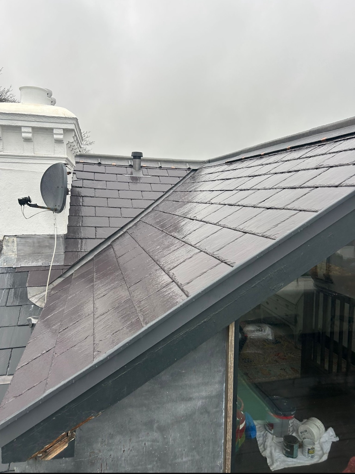 The image shows multiple rooftops with dark gray shingles, a satellite dish, a vent pipe, and a white chimney, under an overcast sky.