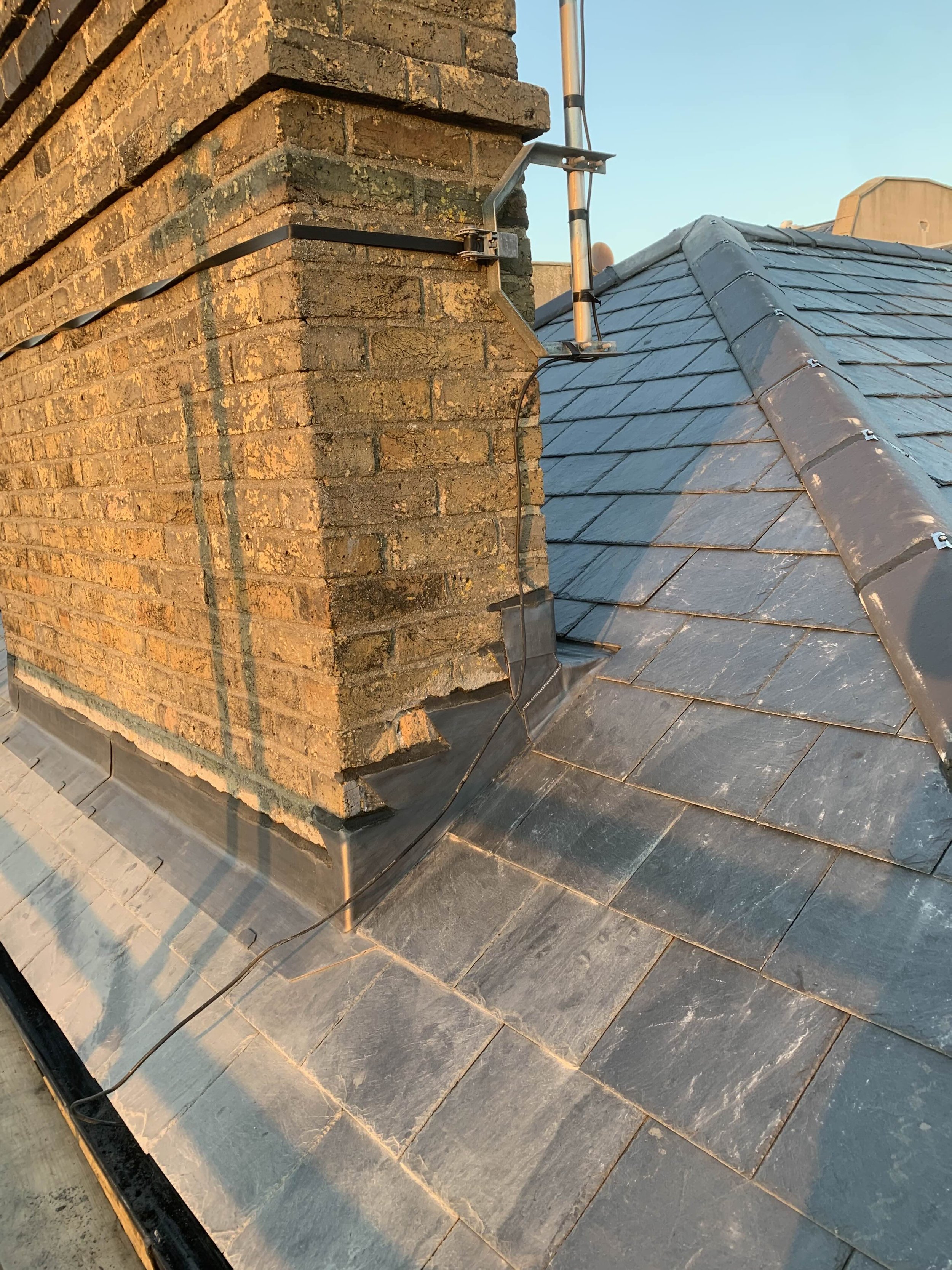 Close-up view of a chimney on a tiled roof, with a metal antenna and electrical wiring attached.