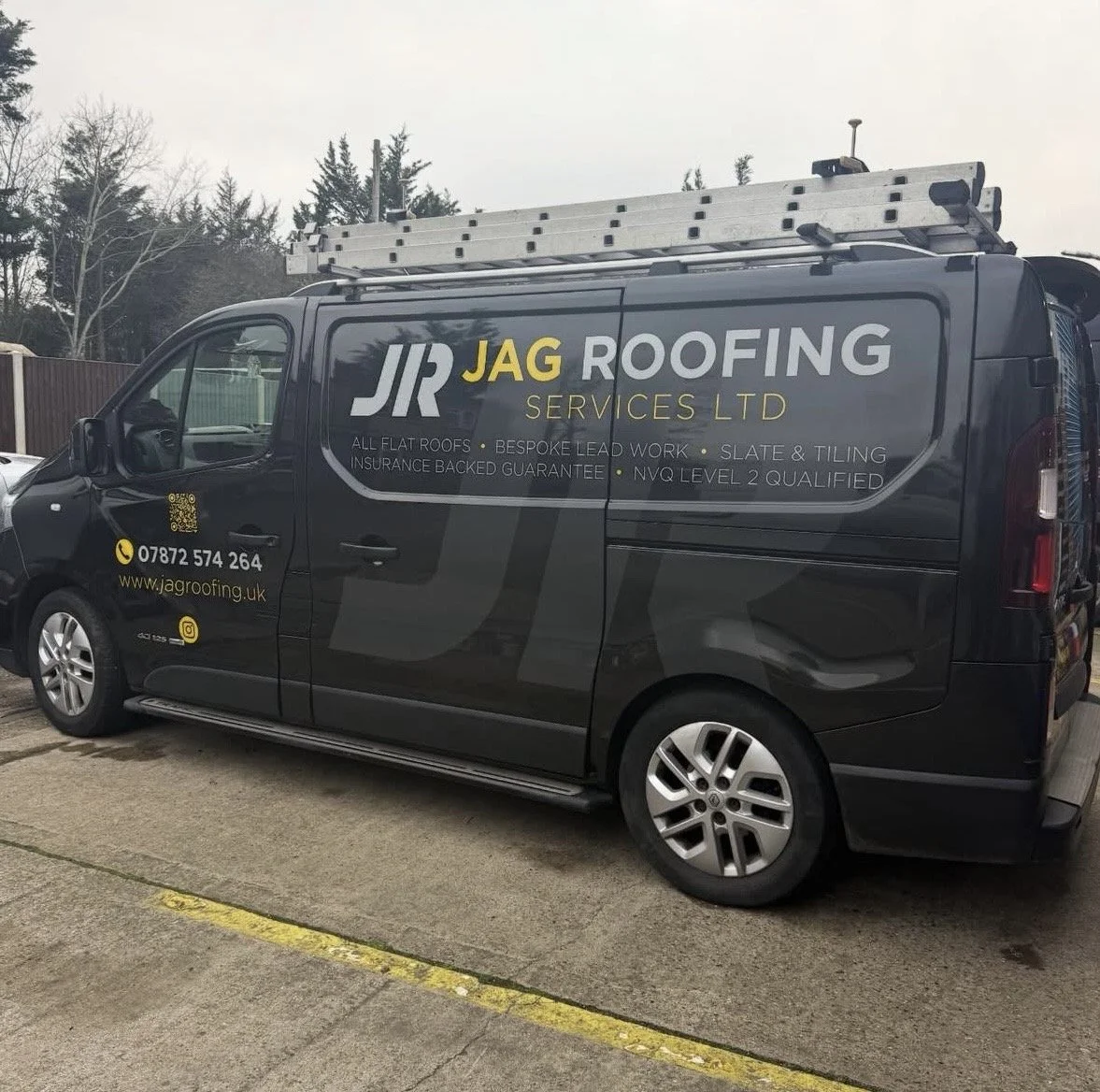 Black company van with yellow and gray lettering for JR JAG Roofing Services LTD, parked on a street with a ladder on top.