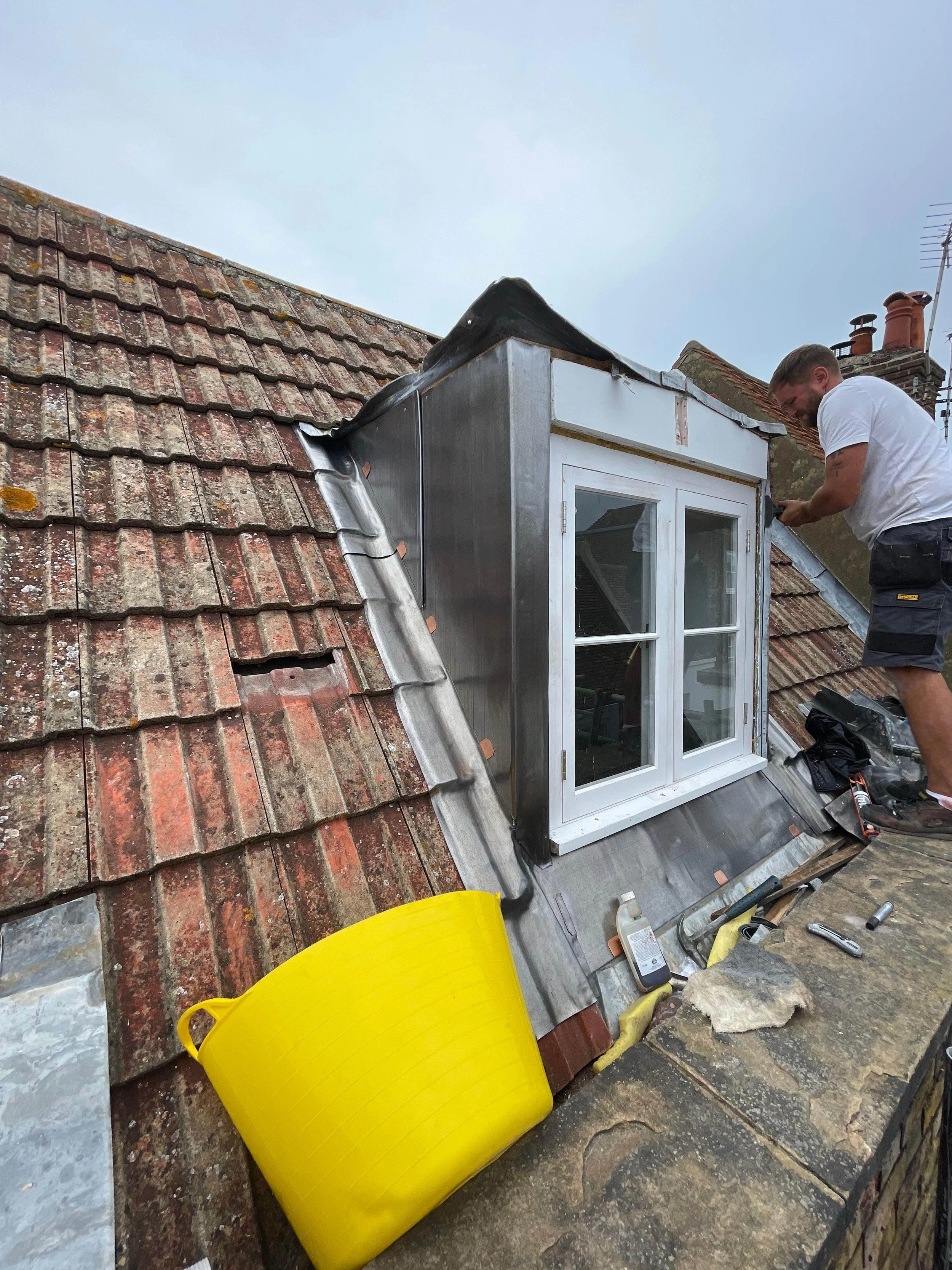 Person working on roof with window installation, tools, and supplies nearby.