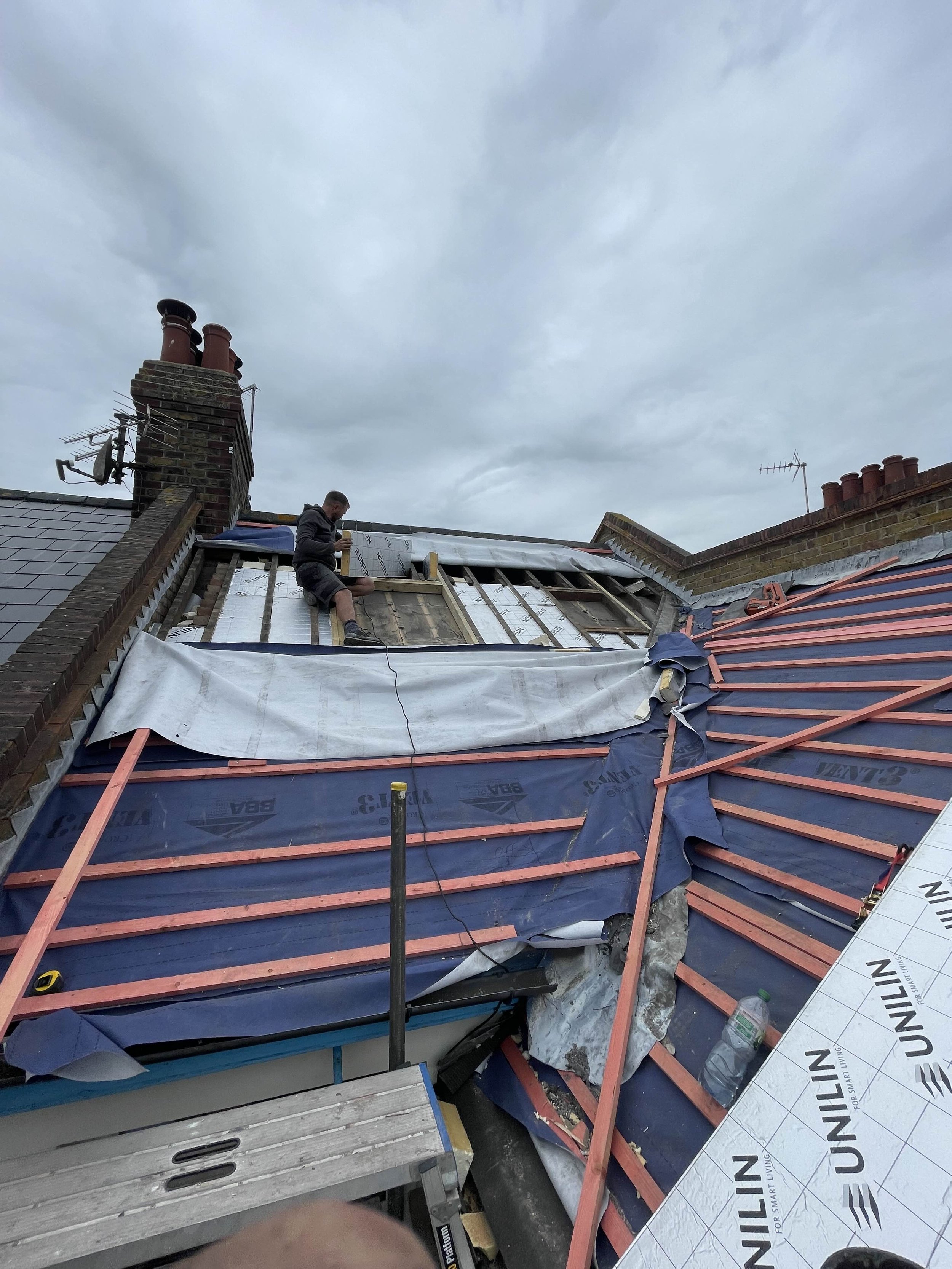 A person working on a roof under cloudy skies, installing or repairing roofing materials.
