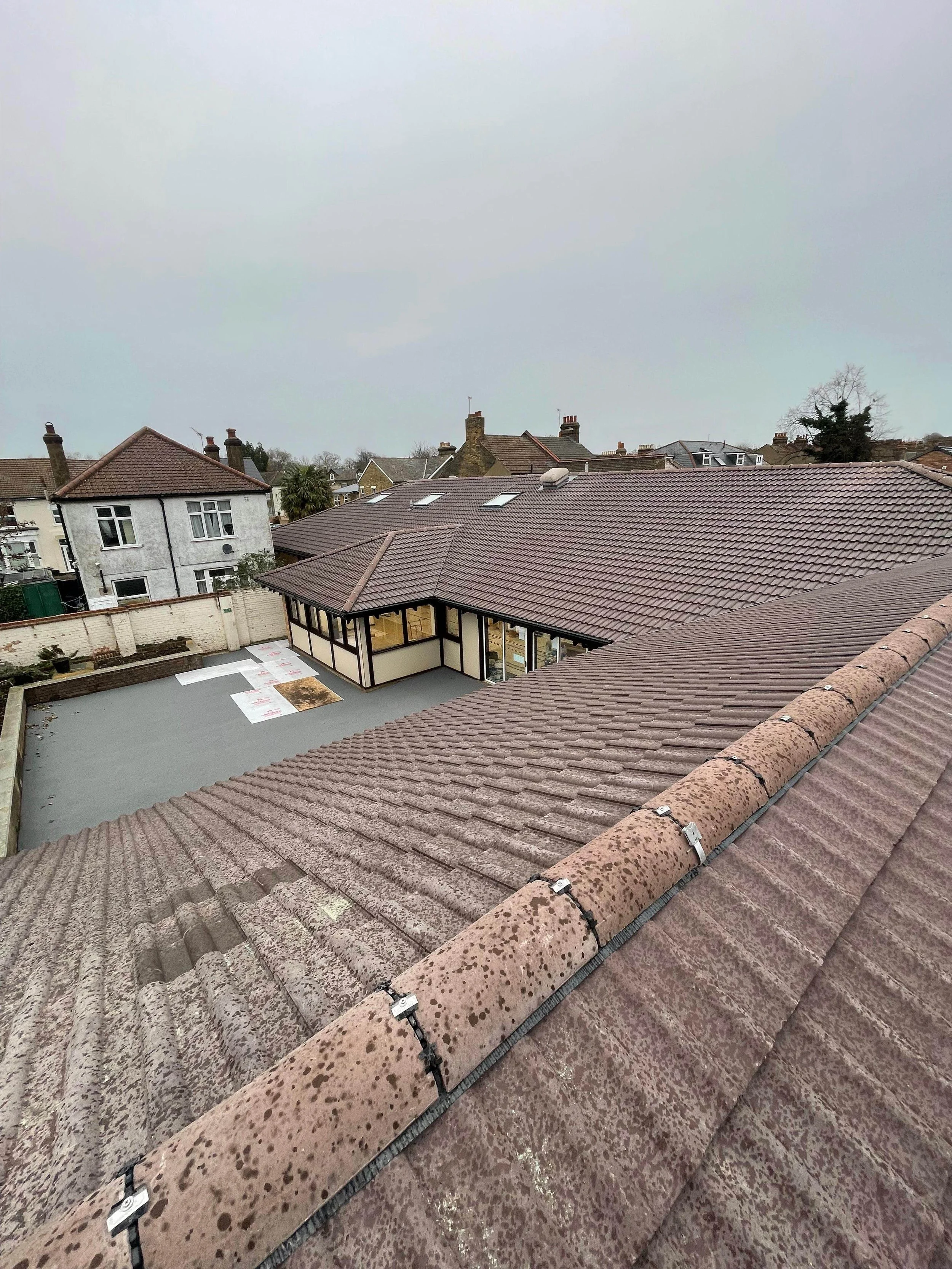 View from a rooftop showing neighboring houses and a large building with a patio area, overcast sky.