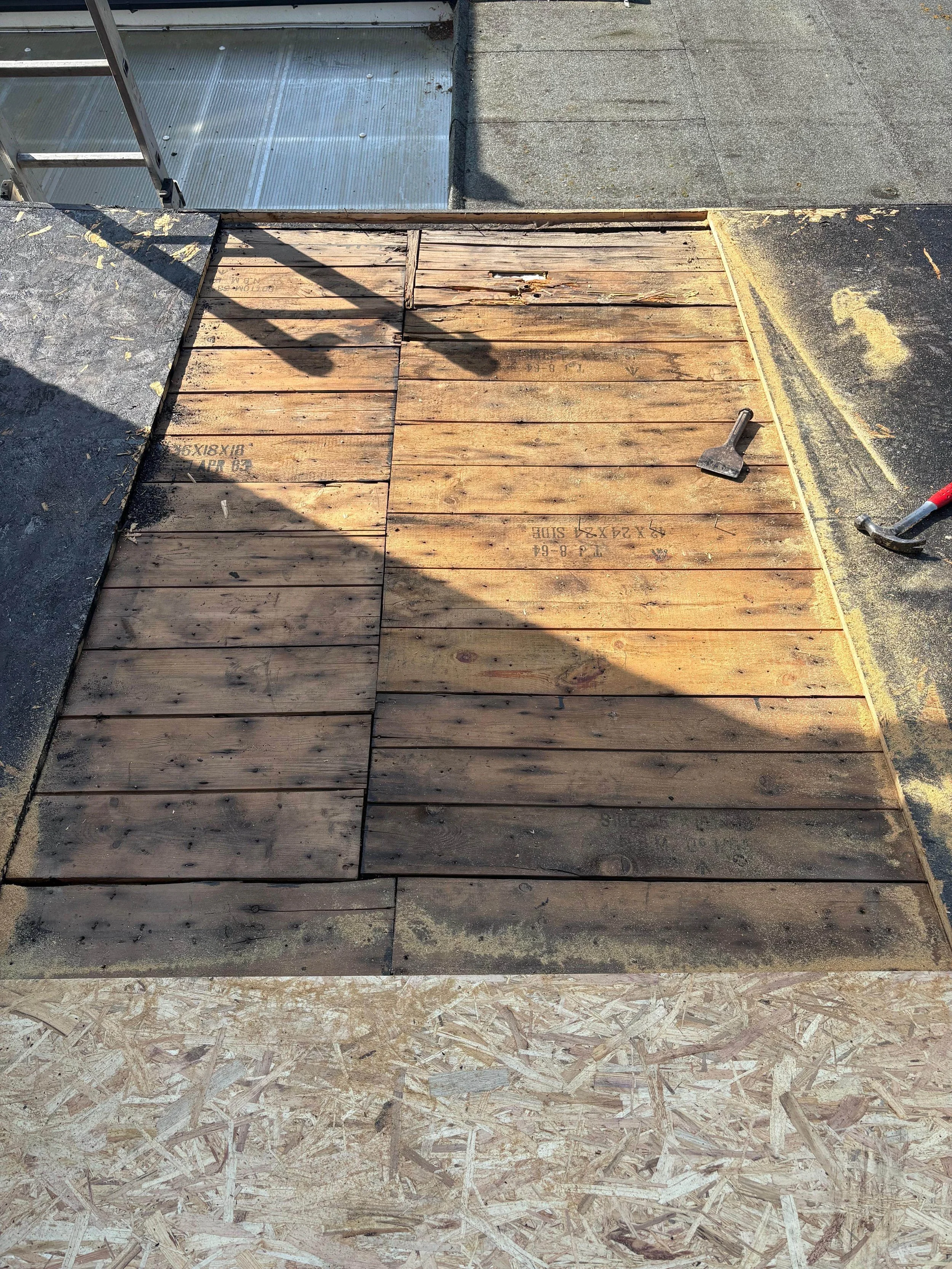 Wooden flooring under construction on a rooftop with some tools and shadows visible.