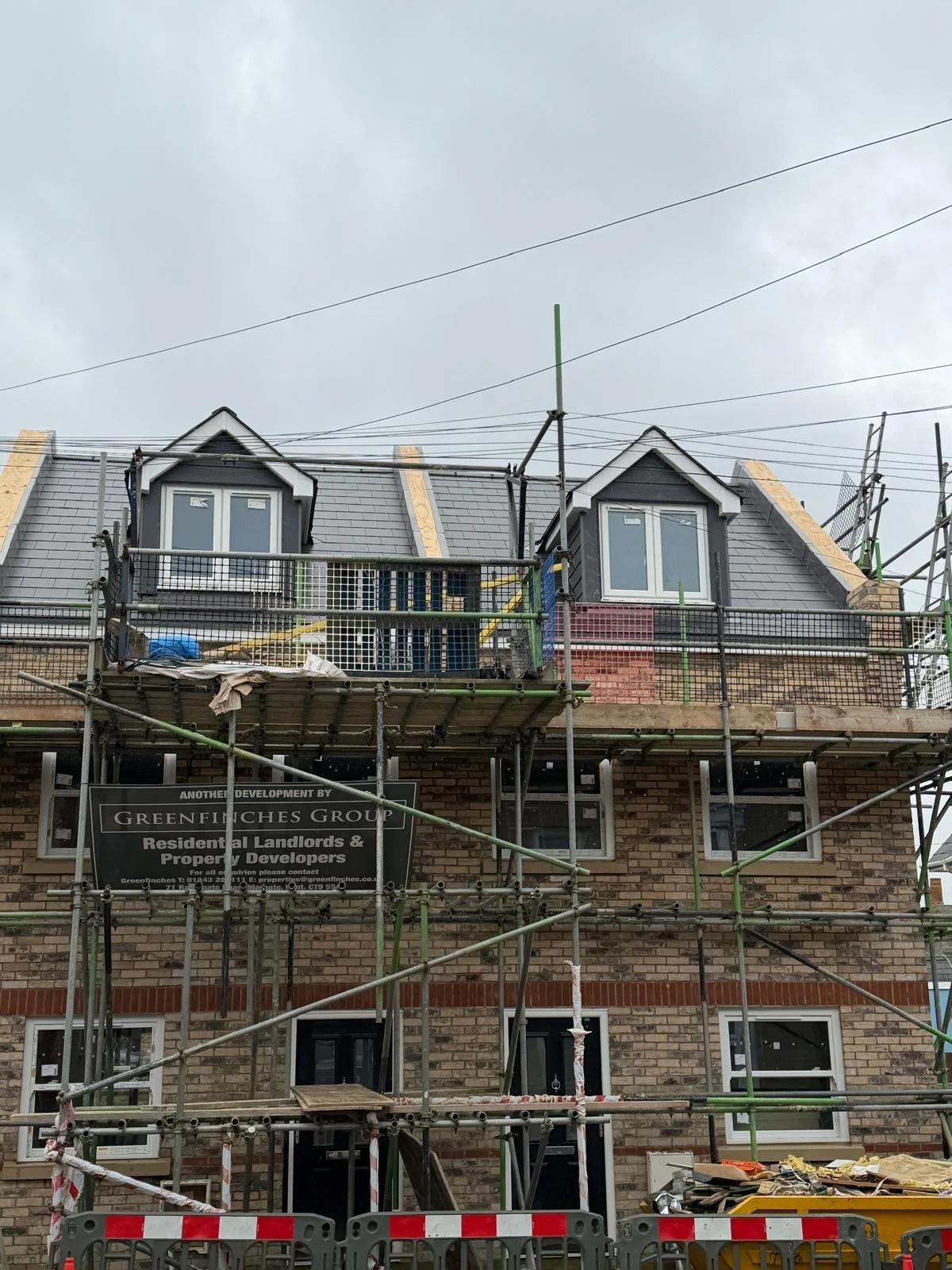 Construction site of a multi-story brick building with scaffolding and new windows being installed, overcast sky.