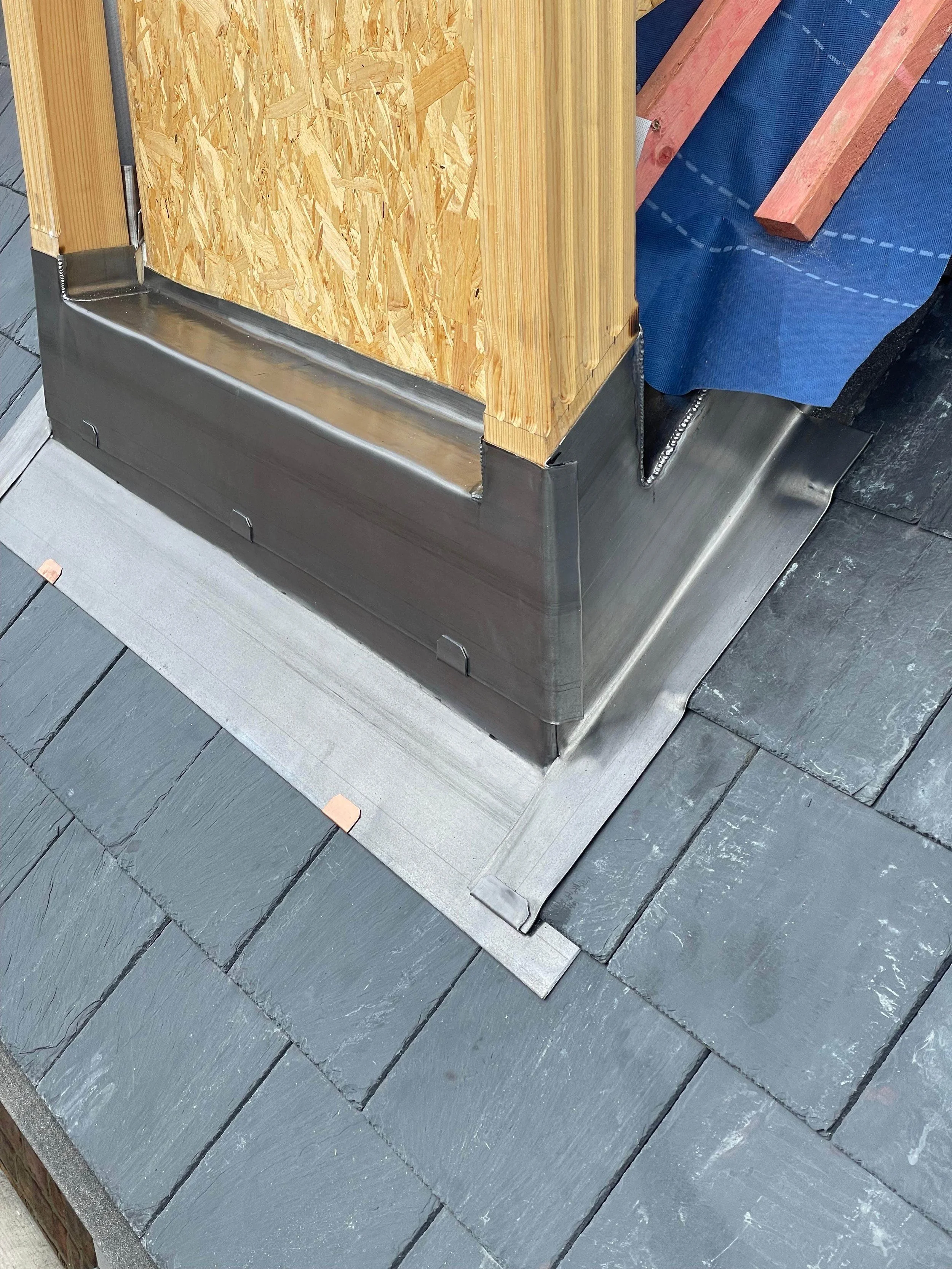 Close-up view of a building corner with metal flashing installed at the base of a wooden structure, on a slate roof.