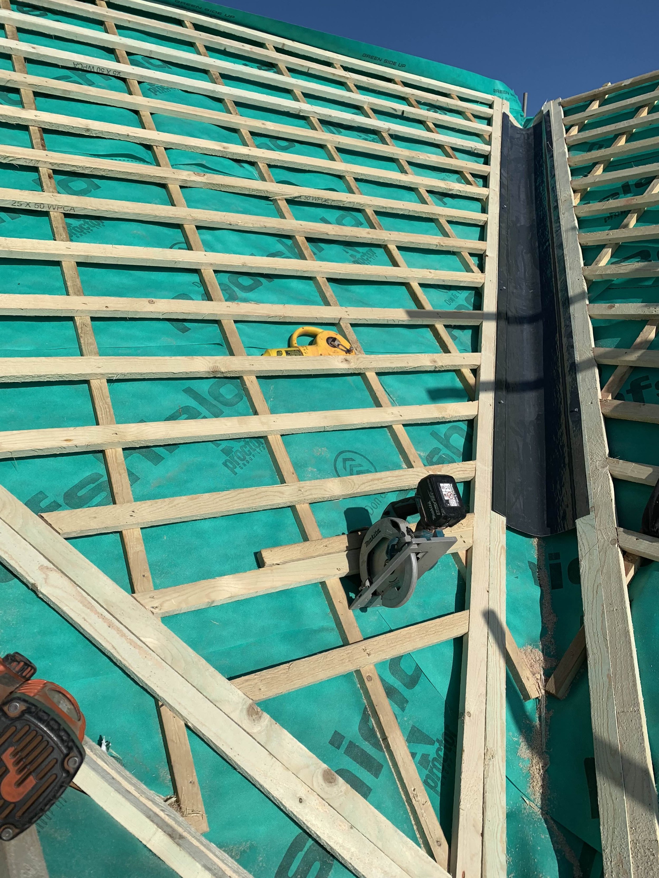 Construction site with wooden framing and green insulation under a clear blue sky.