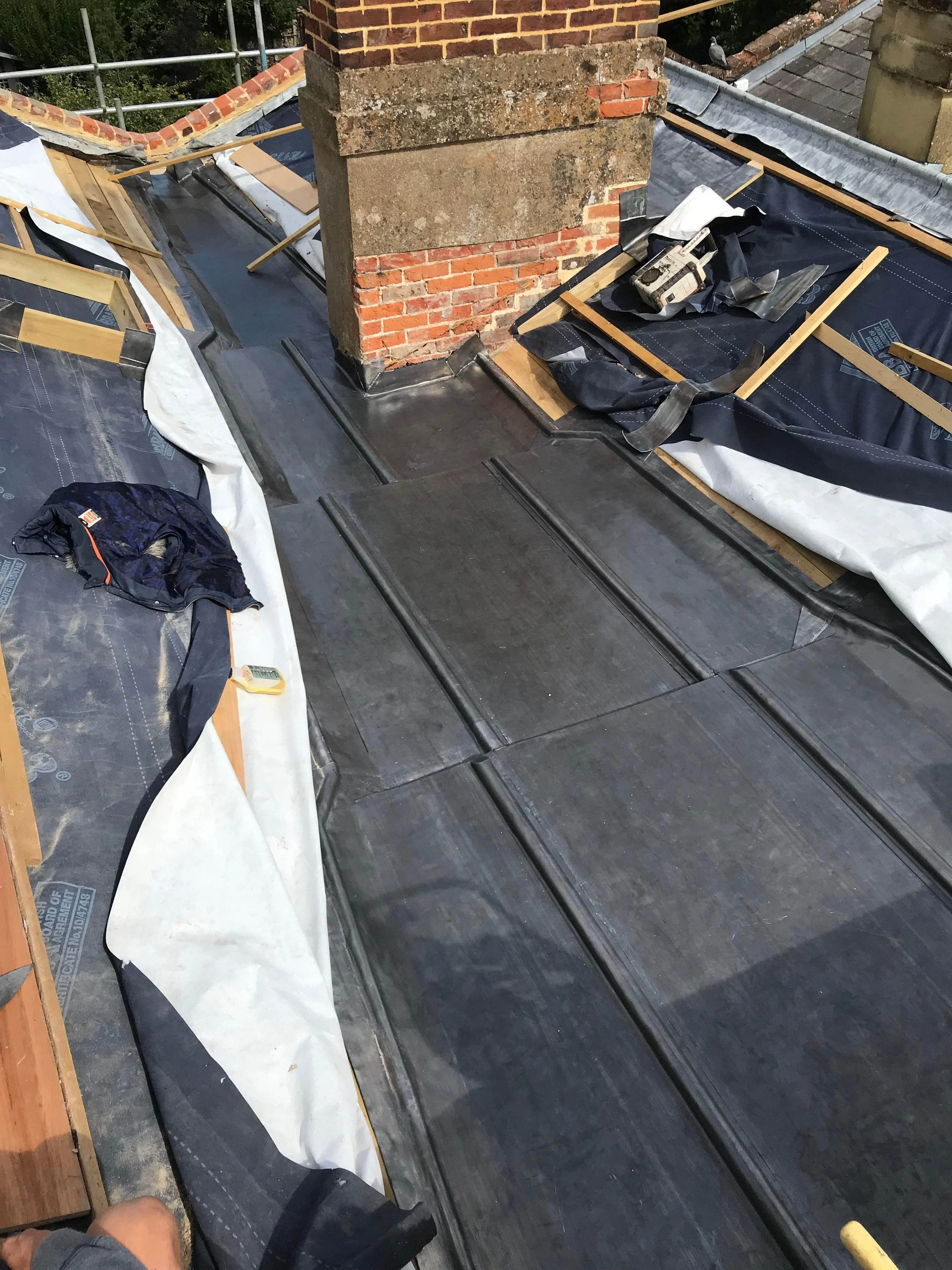 Roof construction site showing weatherproof barrier, roofing materials, wooden battens, and a brick chimney.