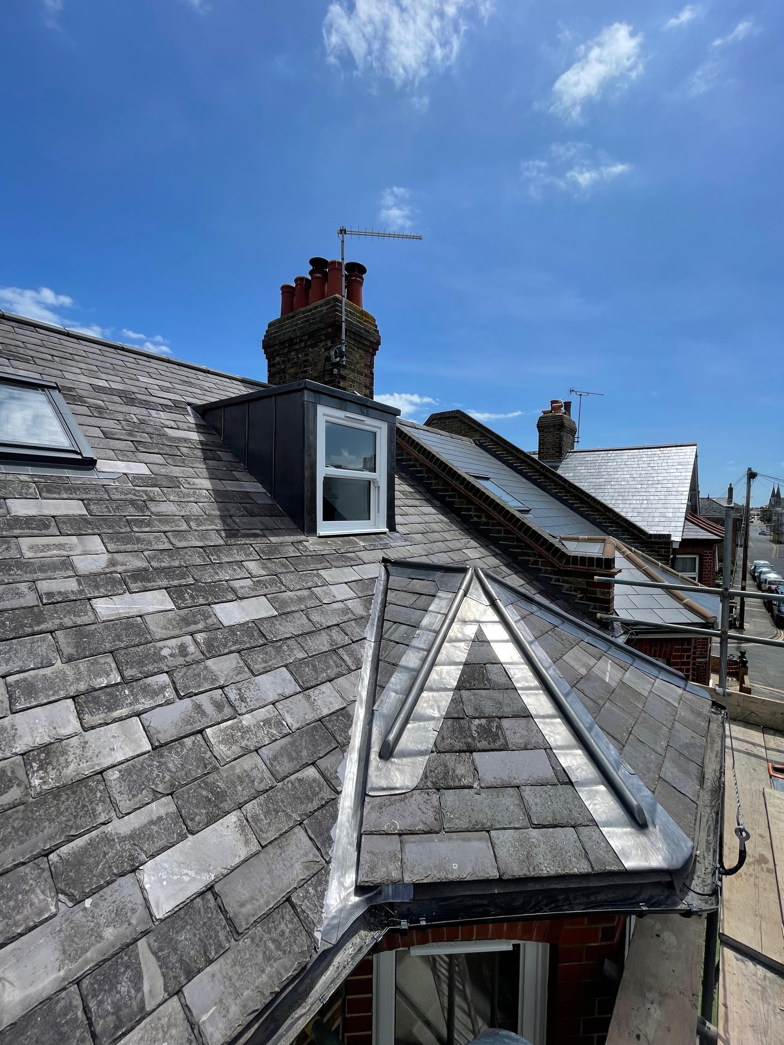 Roof with skylights, a chimney with multiple red chimney pots, and some solar panels under a blue sky with clouds.