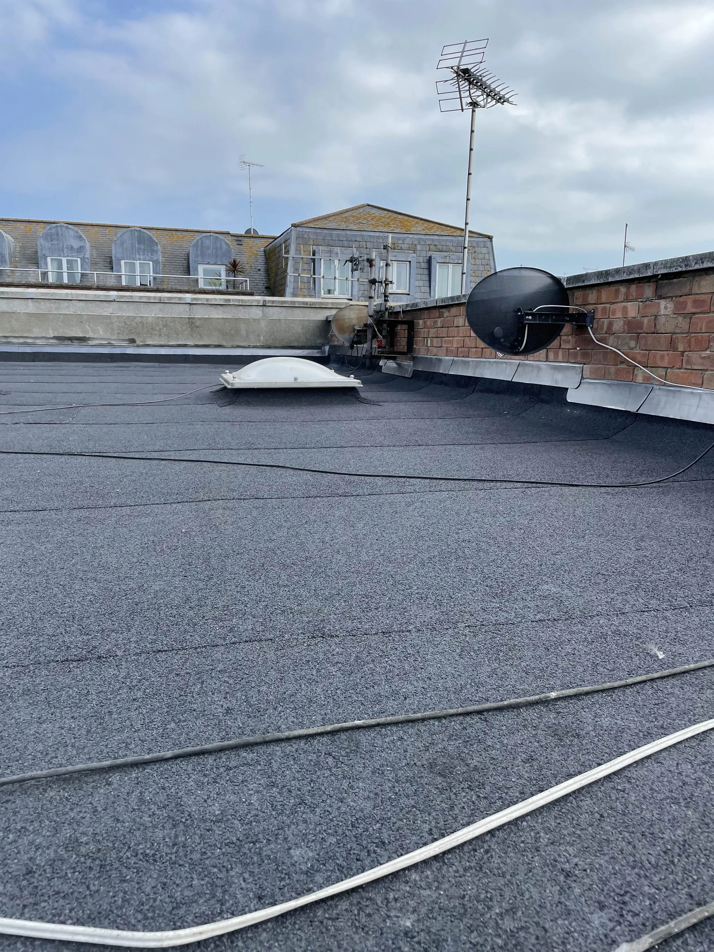 View of a rooftop with antennas, satellite dishes, and a skylight, against a cloudy sky.
