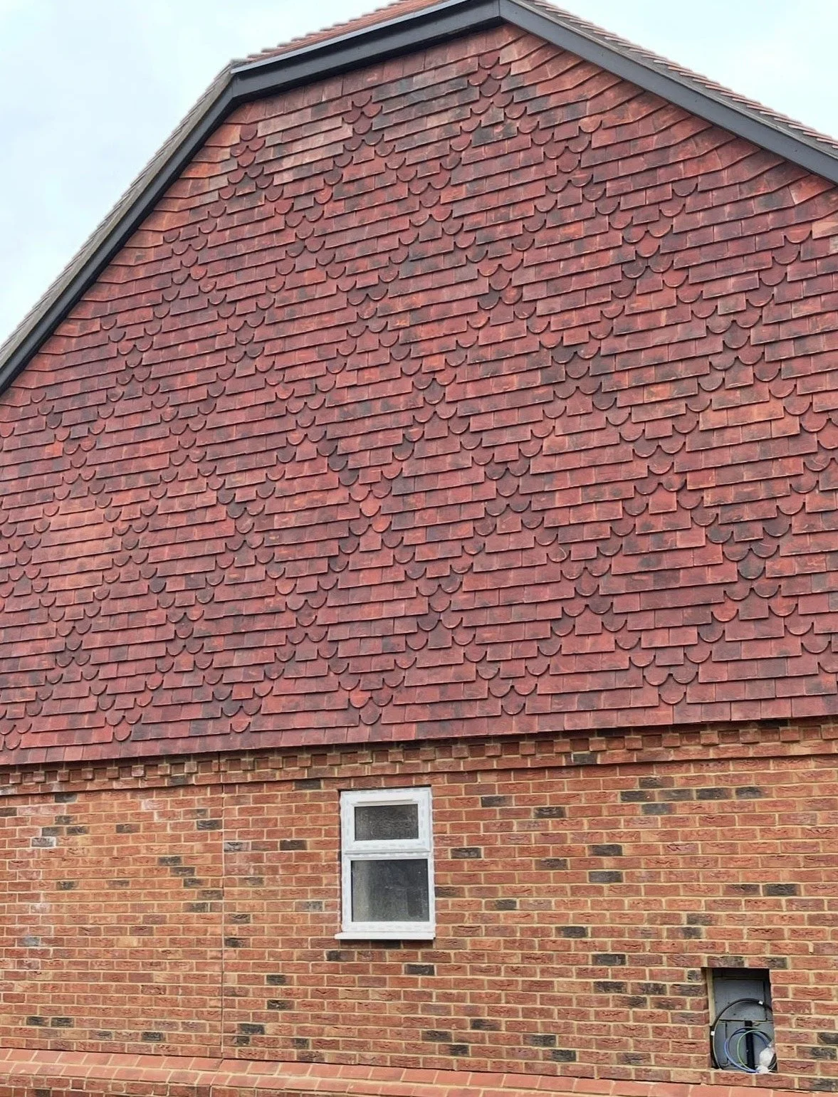 Close-up of house exterior showing brick wall and shingles sectioned with small window, and an opening revealing wiring.